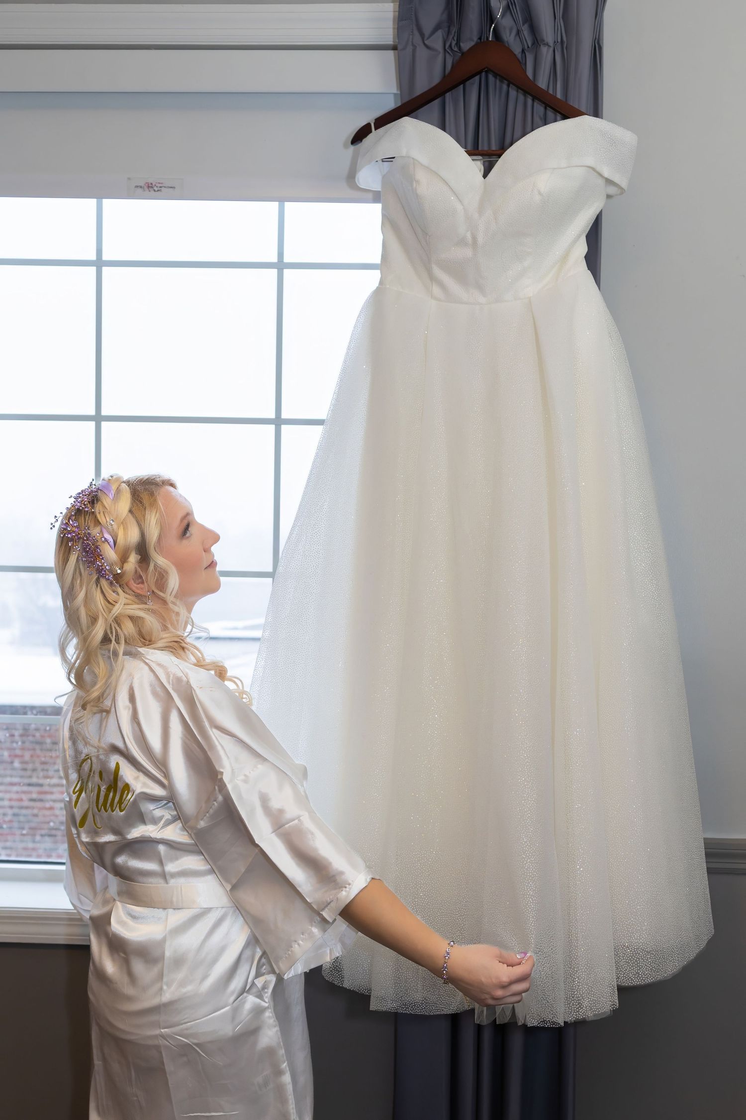 White tulle wedding dress hanging by a bright window.