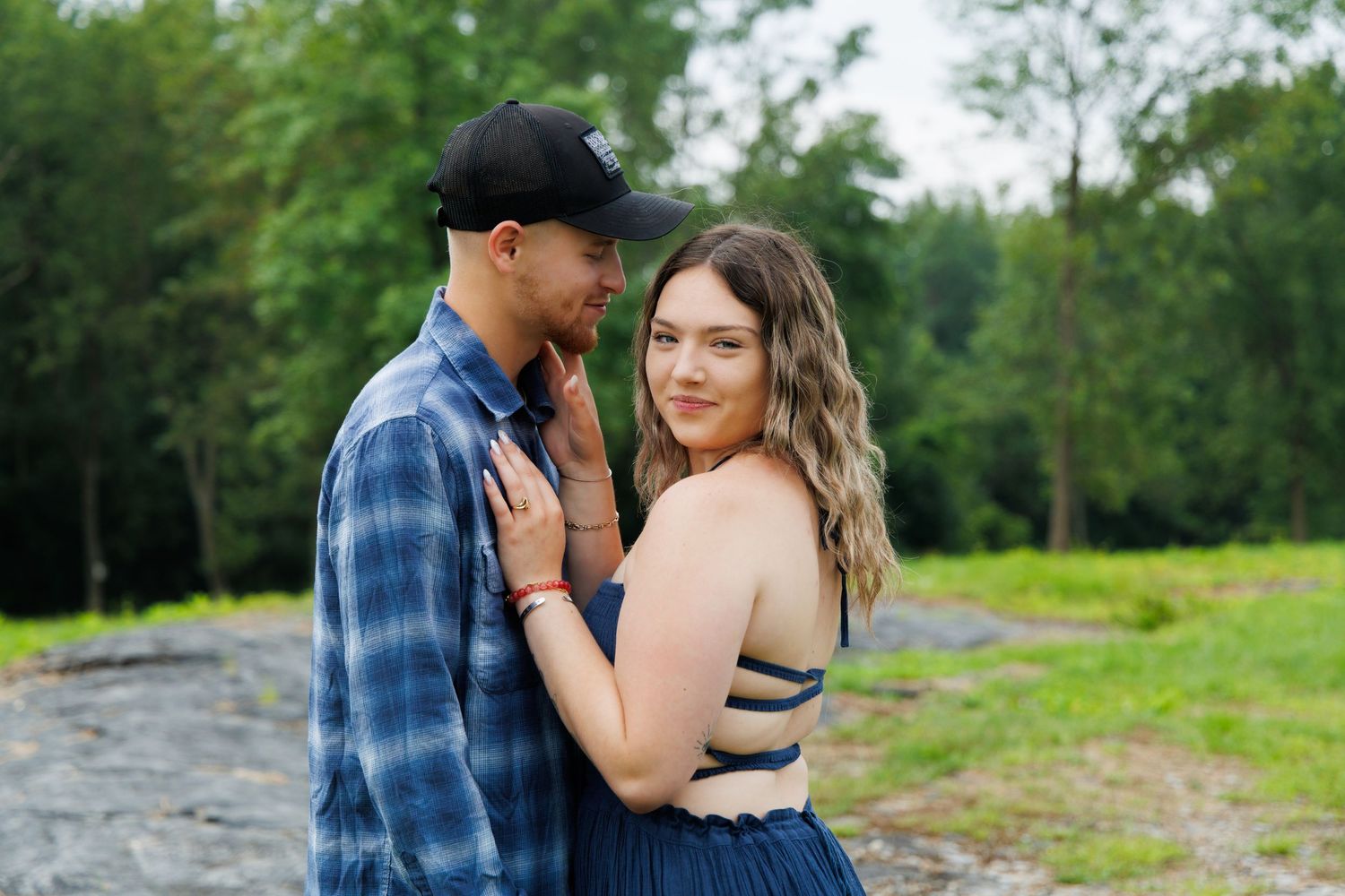 A couple poses romantically in a green field wearing casual attire.