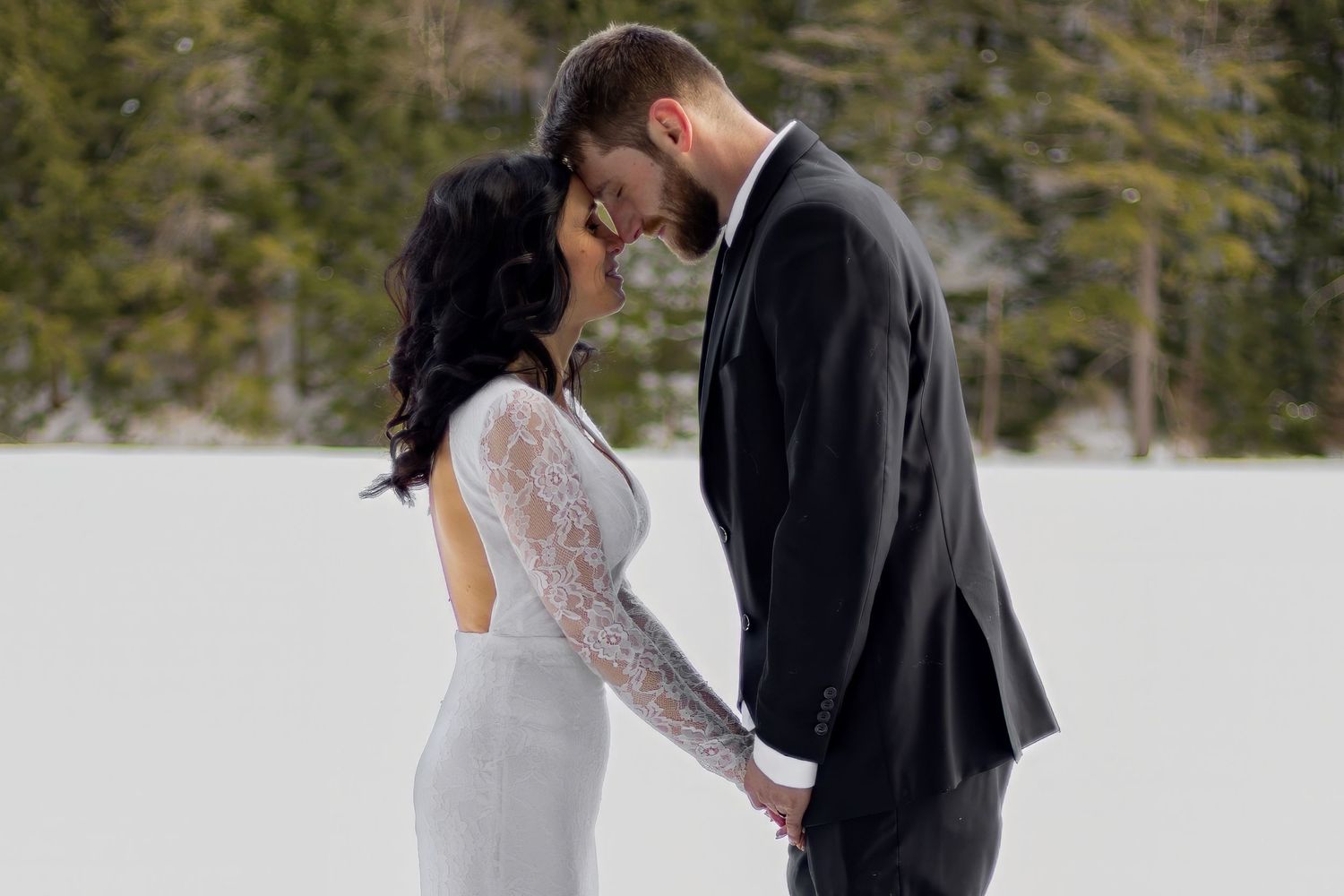 Winter wedding couple standing together in snowy mountain landscape.