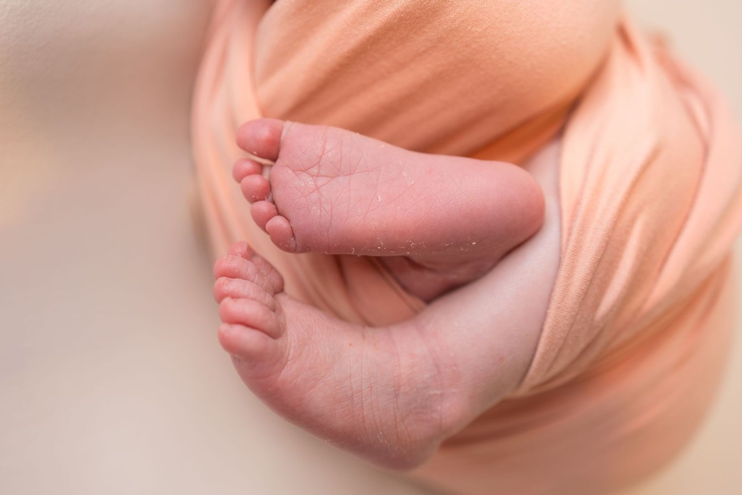 Close-up of newborn baby feet wrapped in a soft peach swaddle blanket, perfect newborn photography.