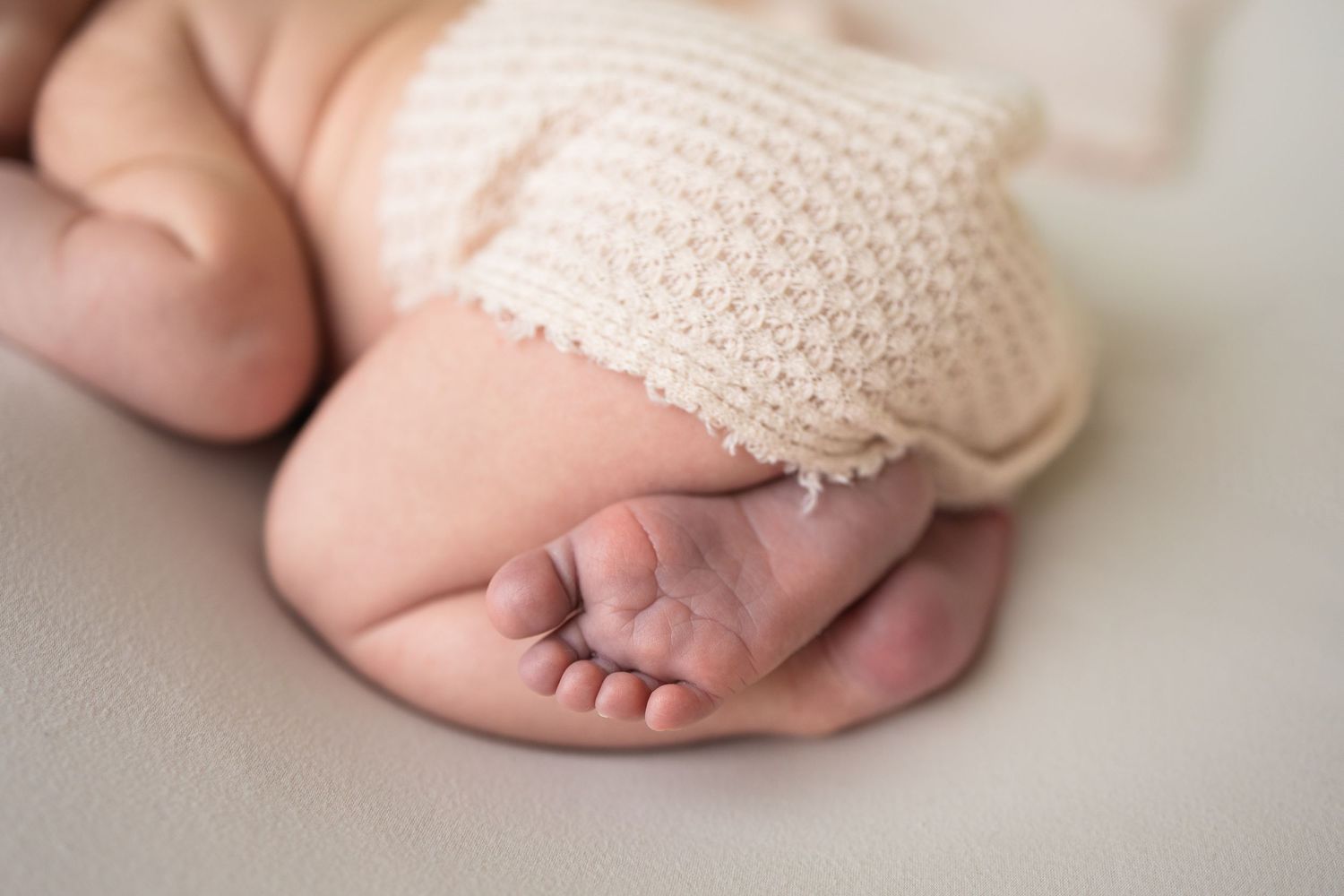 Close-up of tiny newborn baby feet and toes with soft cream knit blanket on white background.