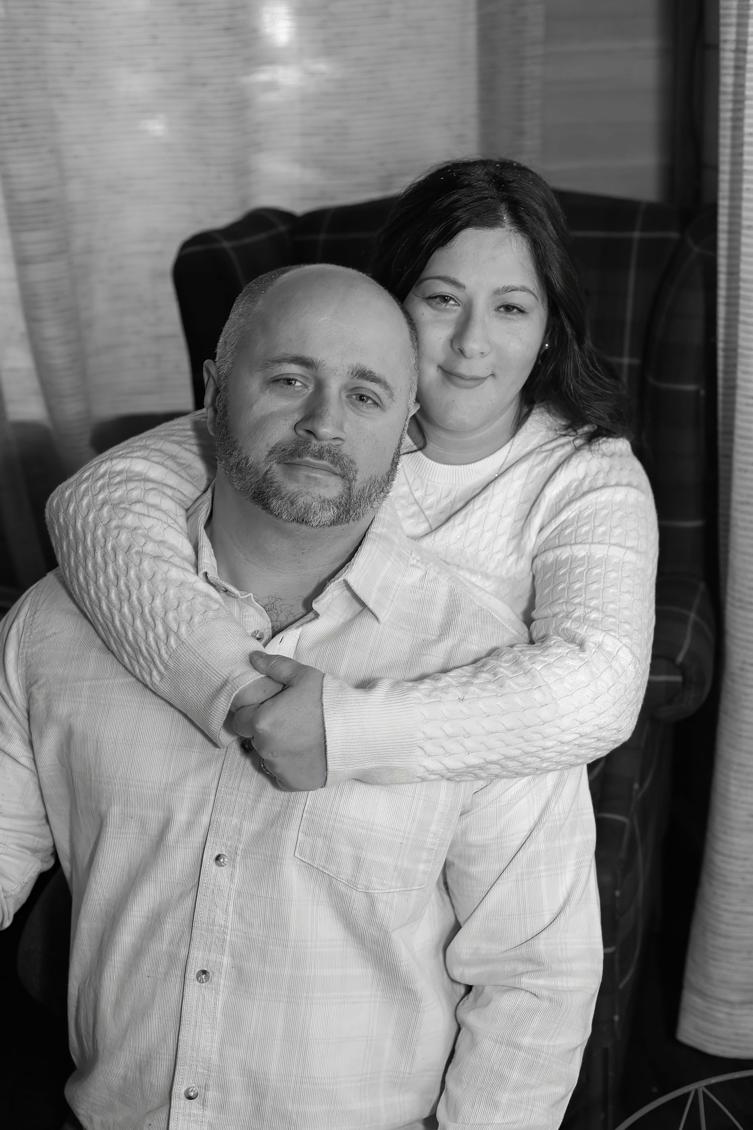 An indoor black and white portrait of a couple in cozy sweaters embracing.