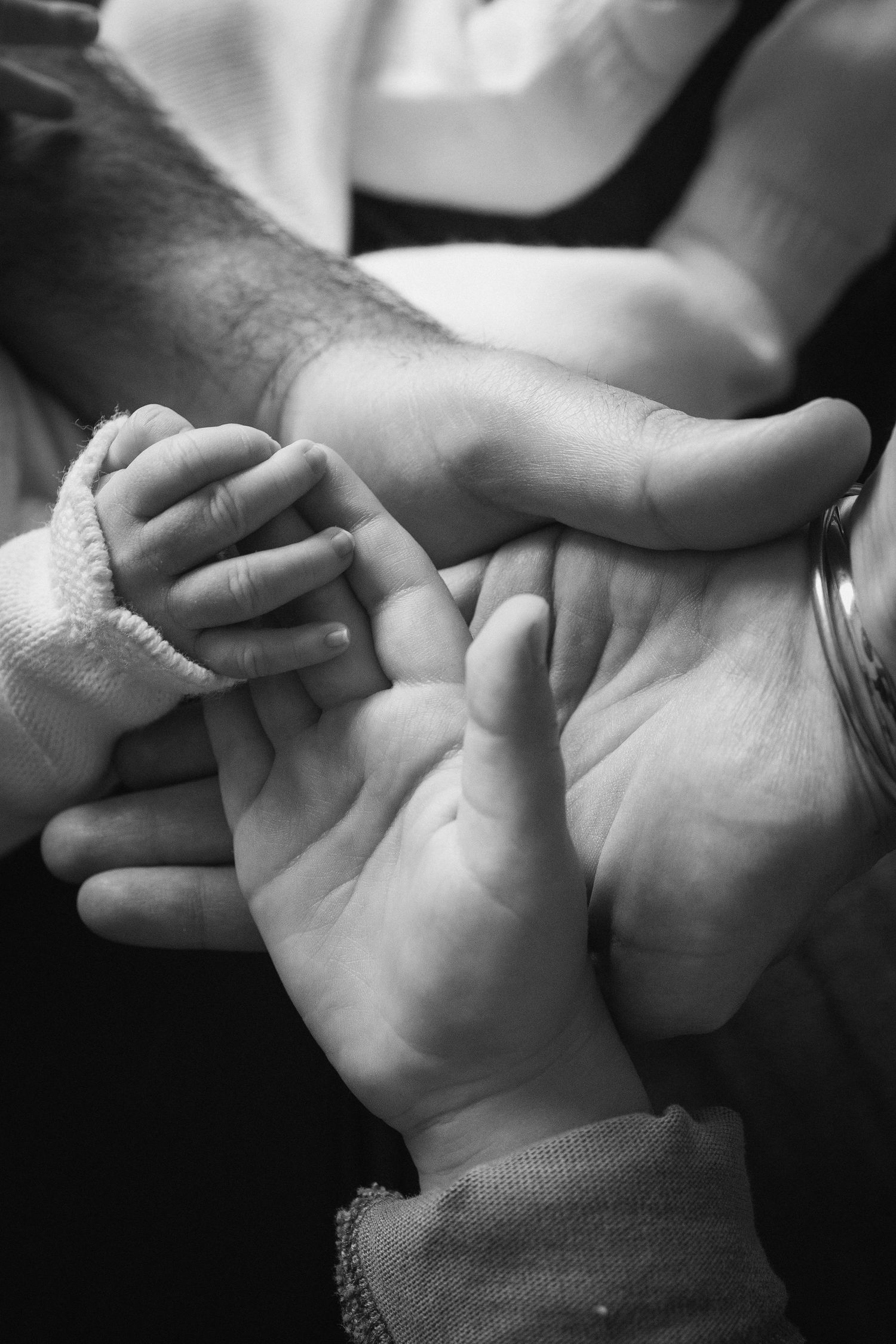 Black and white photo of a baby's tiny hand resting in the open palms of two adults.