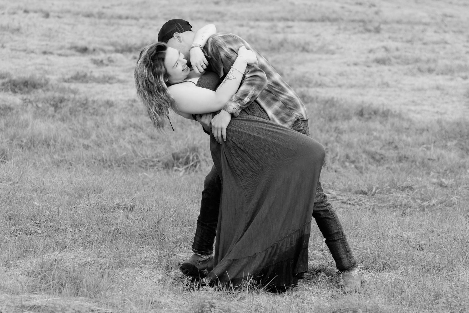 A romantic black and white photo of a couple embracing in a field.