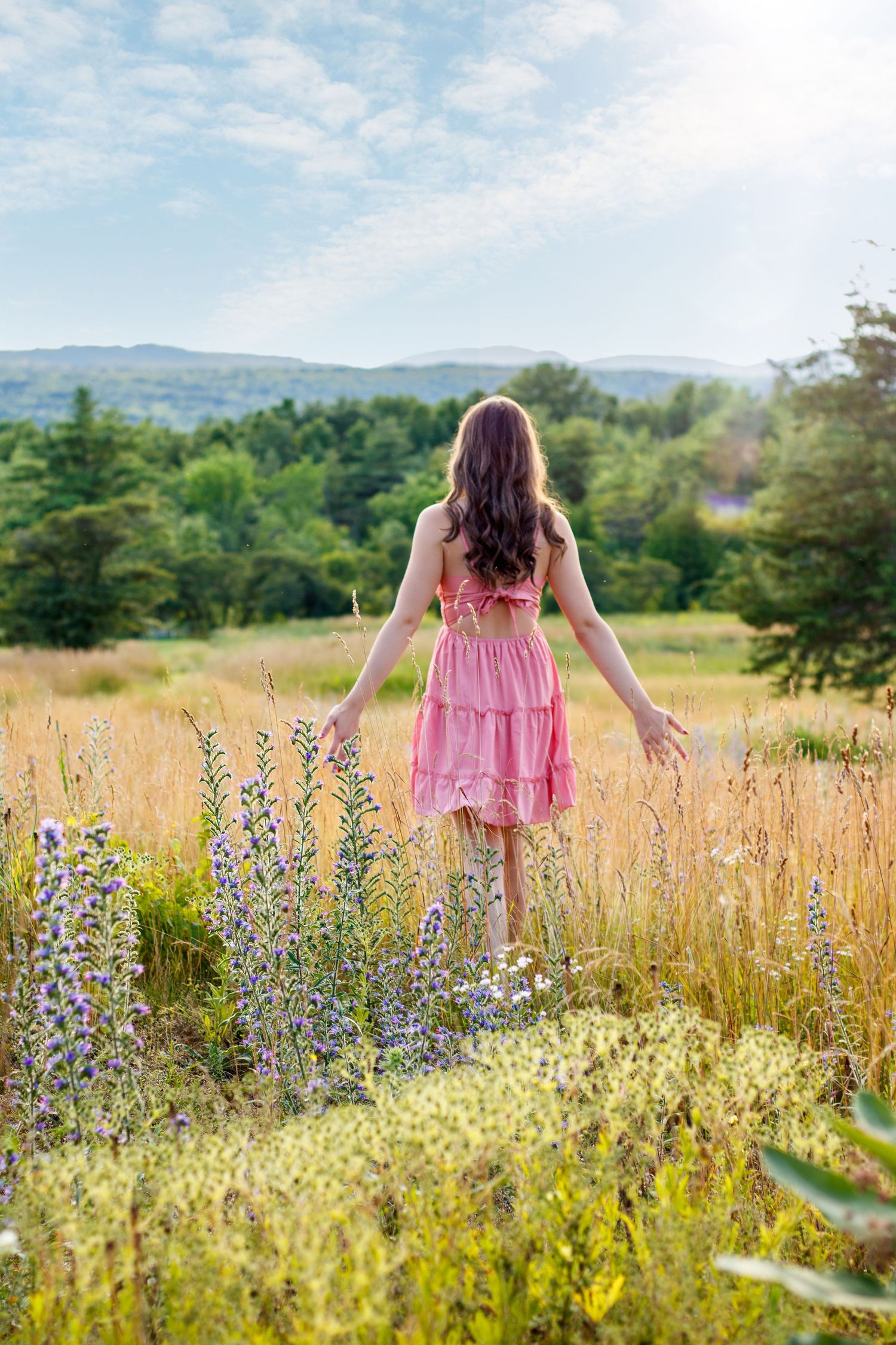 Pink dress flowing in a summer meadow filled with wildflowers and tall grass.
