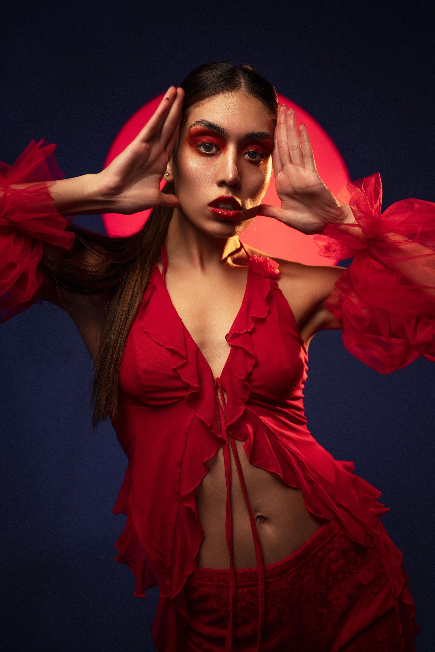 Fashion portrait in vibrant red ruffled dress against dark background with dramatic lighting.