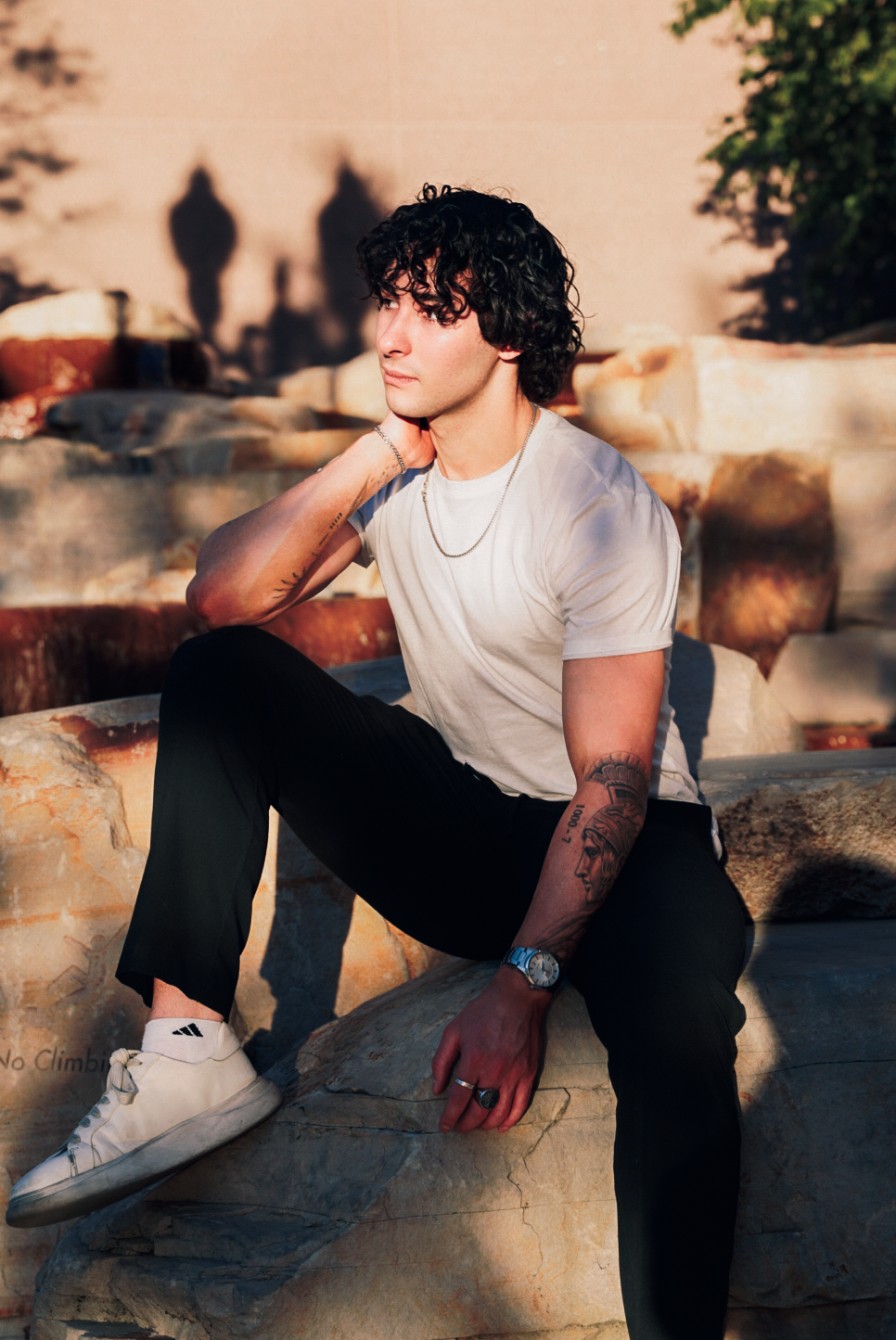 Casual outdoor photoshoot with someone wearing white t-shirt and dark pants sitting on concrete steps at sunset.