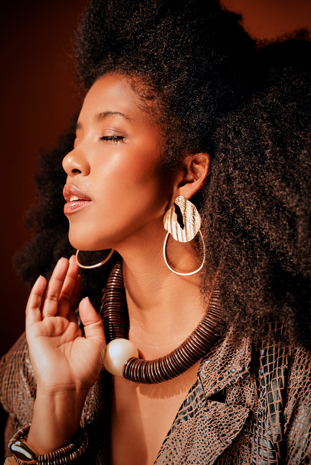 Close-up fashion portrait with statement hoop earrings and textured hair in warm lighting.
