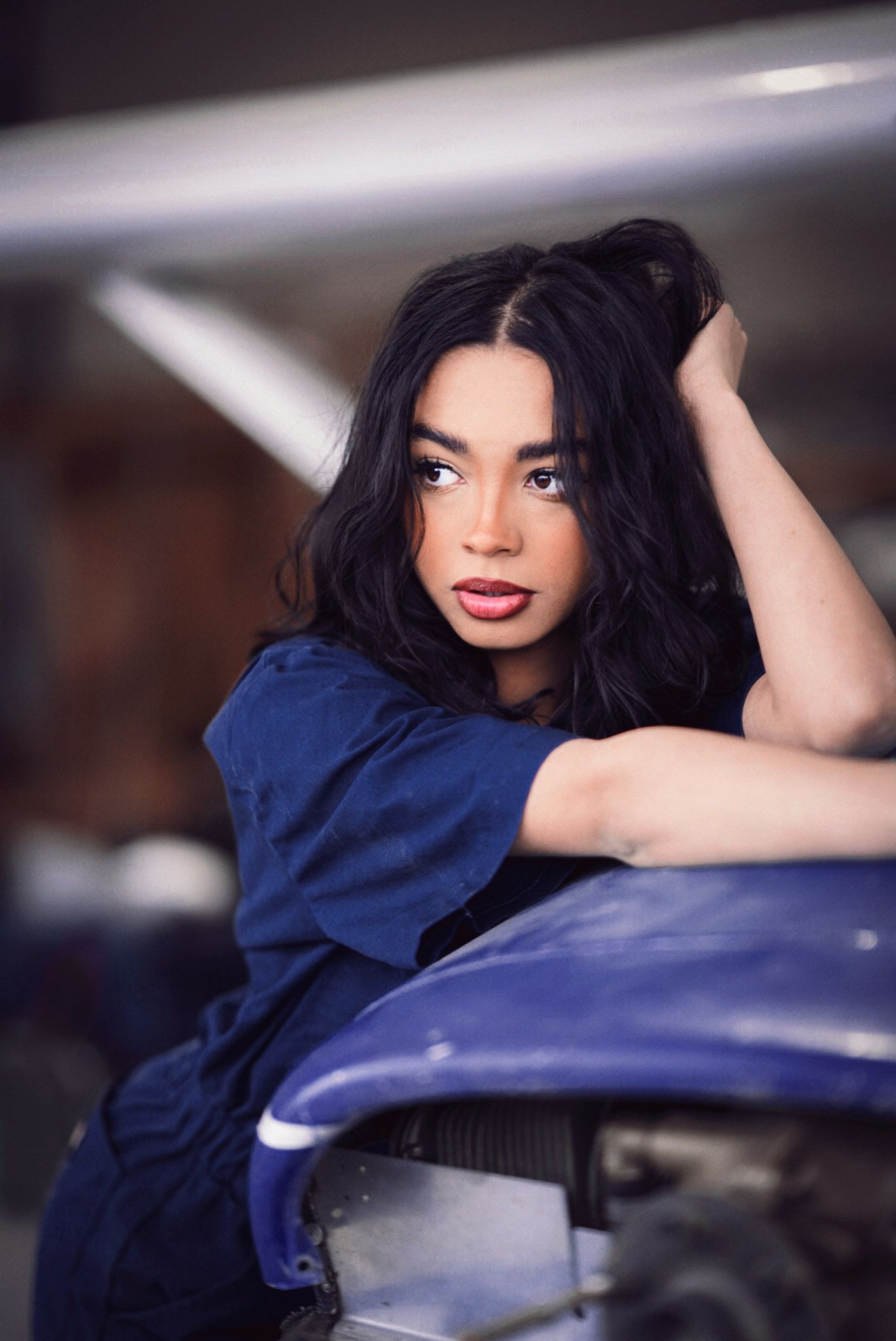 A person in a navy blue top poses playfully against a car in a series of connected artistic photographs.