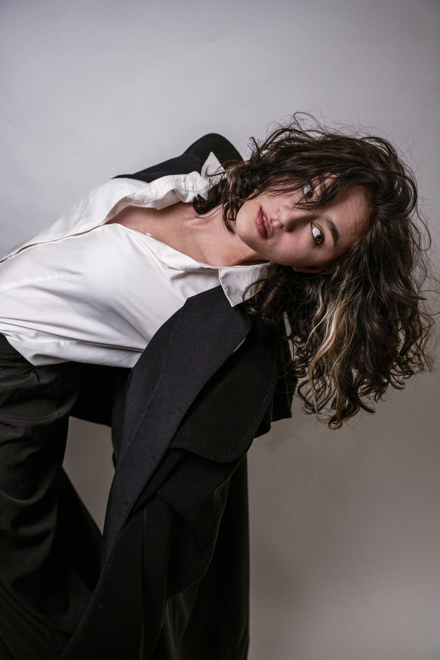 A fashion model in a black blazer and white shirt poses dramatically against a gray background in a series of artistic shots.