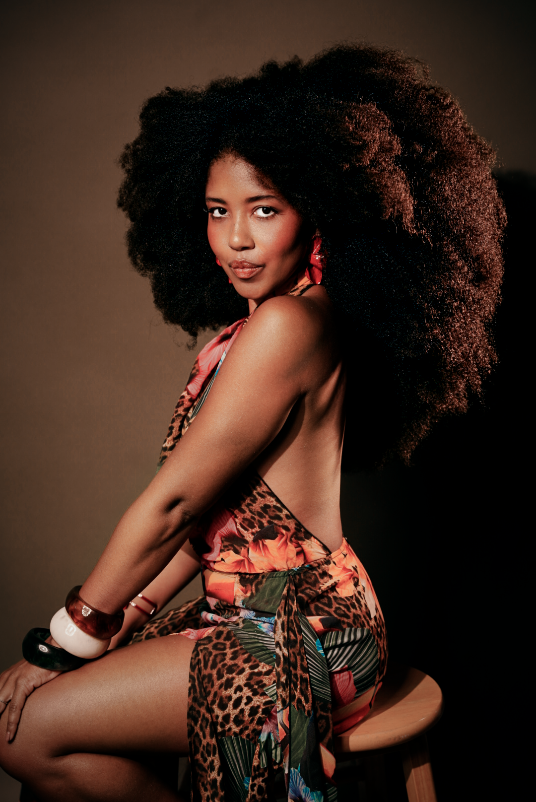 Artistic portrait featuring natural curly hair and animal print clothing against a dark background.