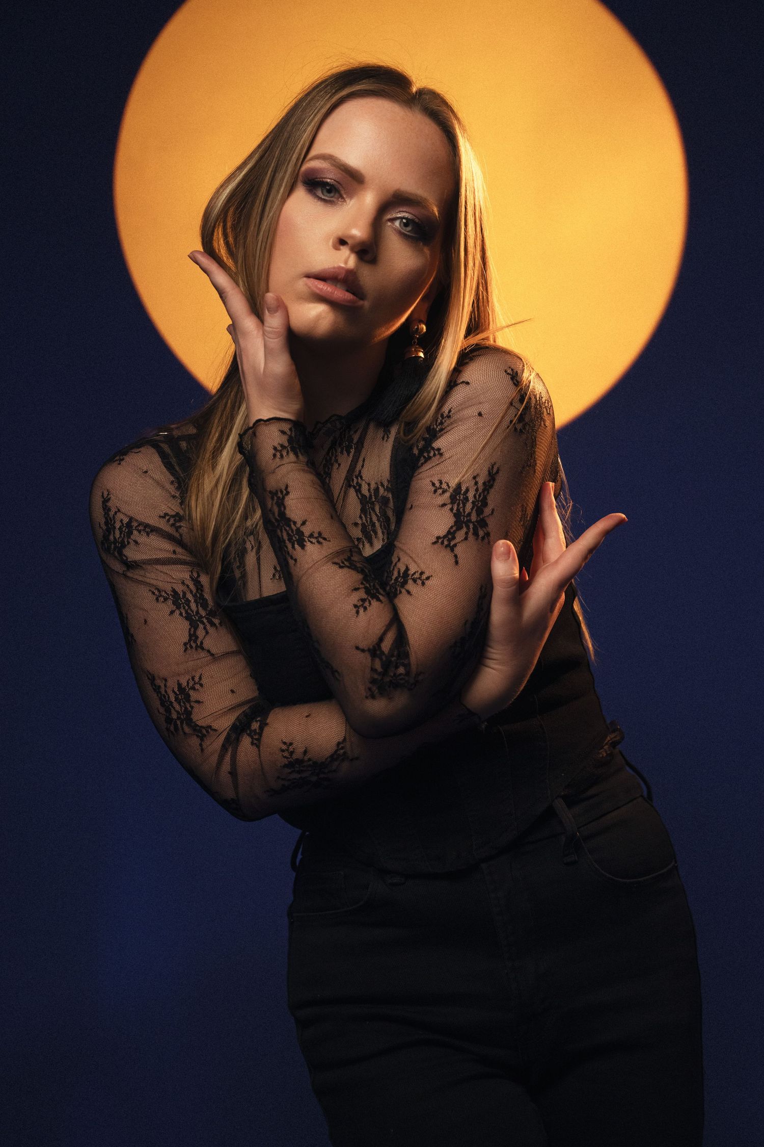 Fashion portrait with dramatic golden backlight showing model in black lace top against dark blue background.