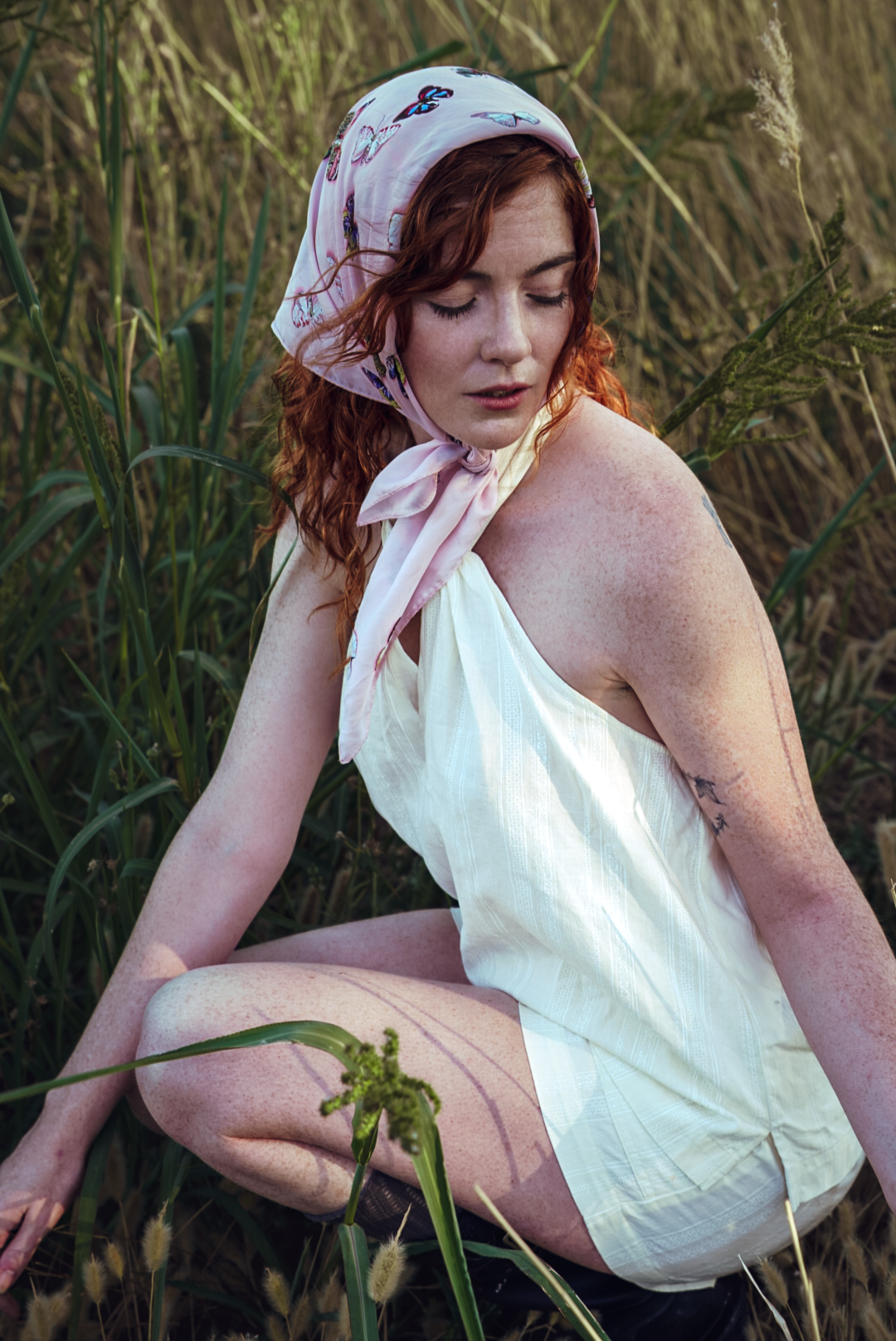Vintage-inspired portrait in white dress among tall grass with natural lighting.