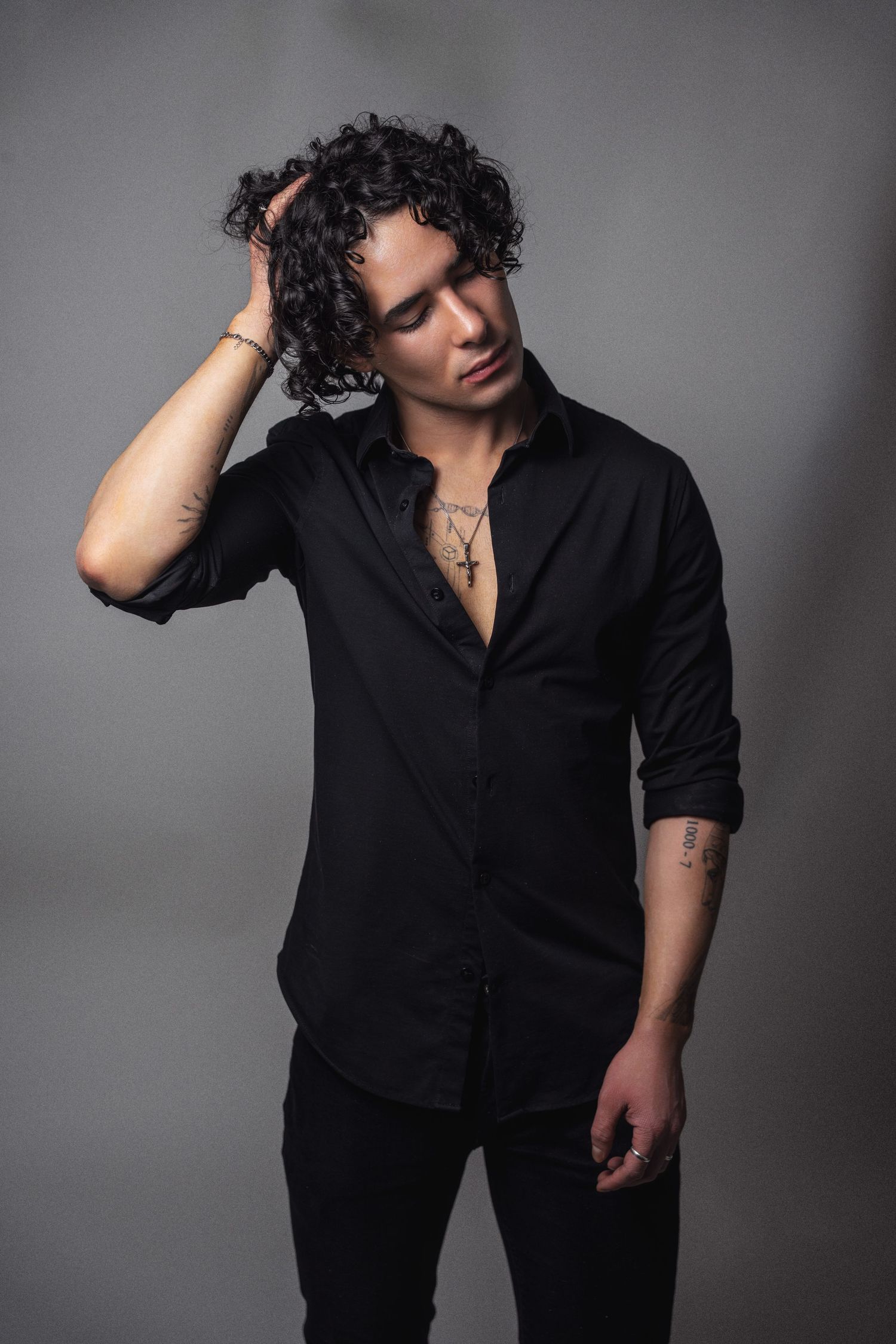 A moody black and white portrait showing a figure in a dark shirt against a gray background.