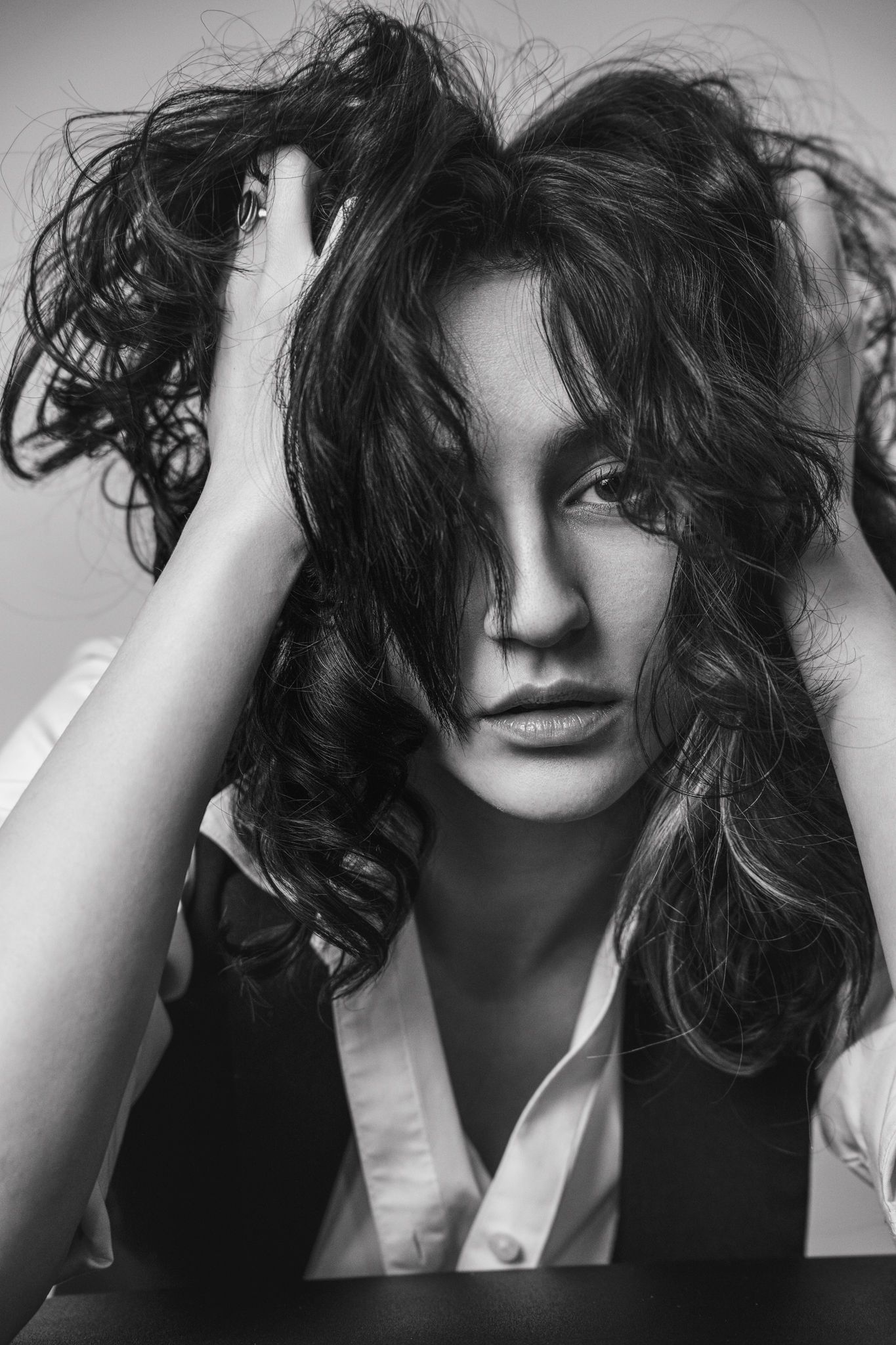 Black and white portrait of someone with wild, tousled dark curly hair wearing a white shirt and dark vest.
