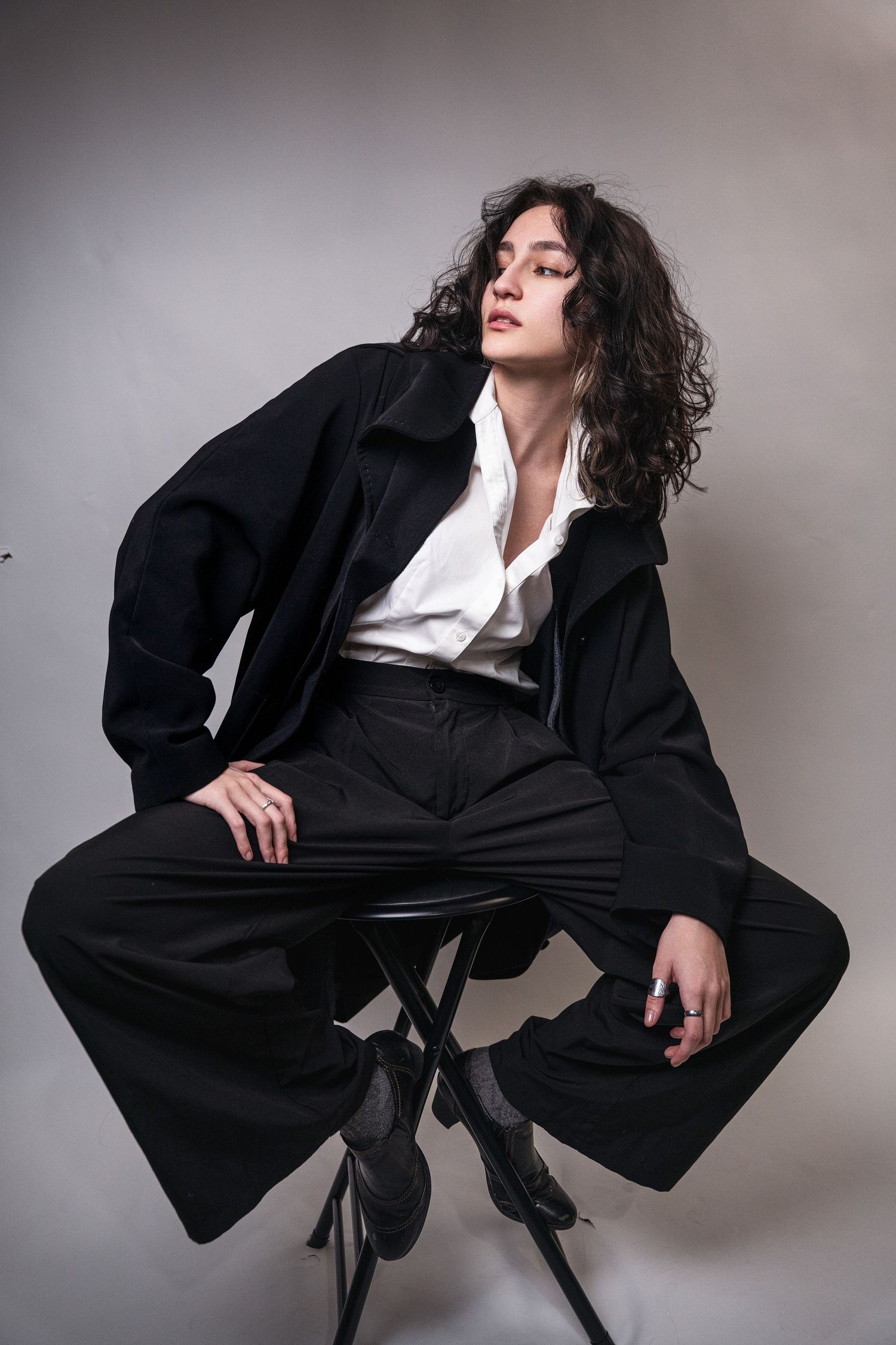 A dramatic fashion pose series featuring a model in an oversized black suit and white shirt against a gray backdrop.