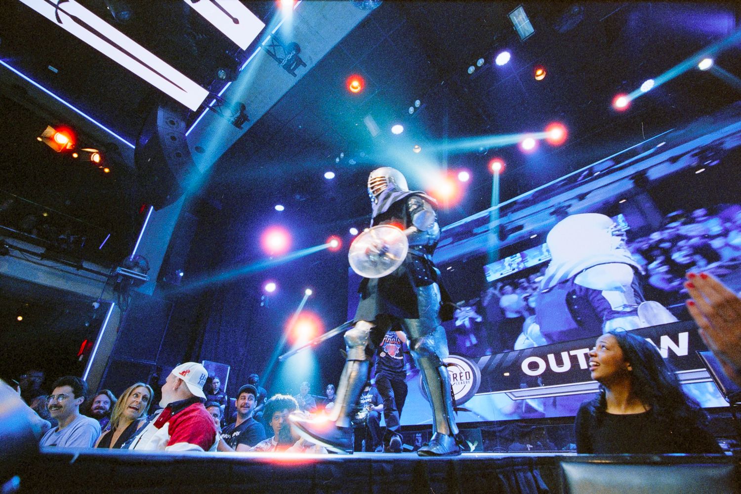 Costumed performer holds glowing orb on stage at a vibrant esports or gaming event with colorful lighting.