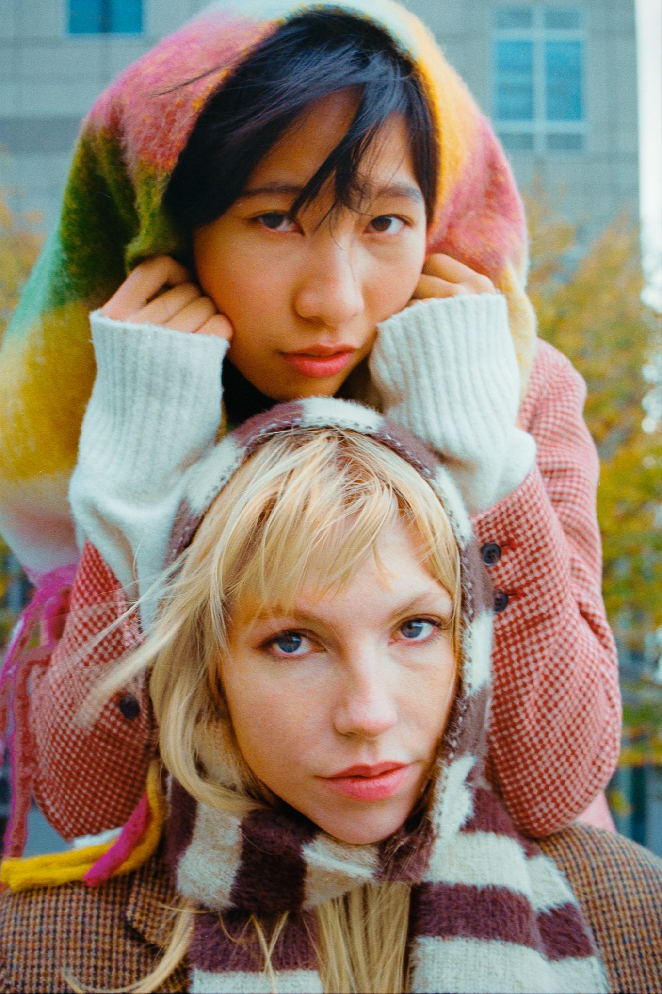 Two models pose together wearing winter accessories and cozy knitwear in an outdoor setting.