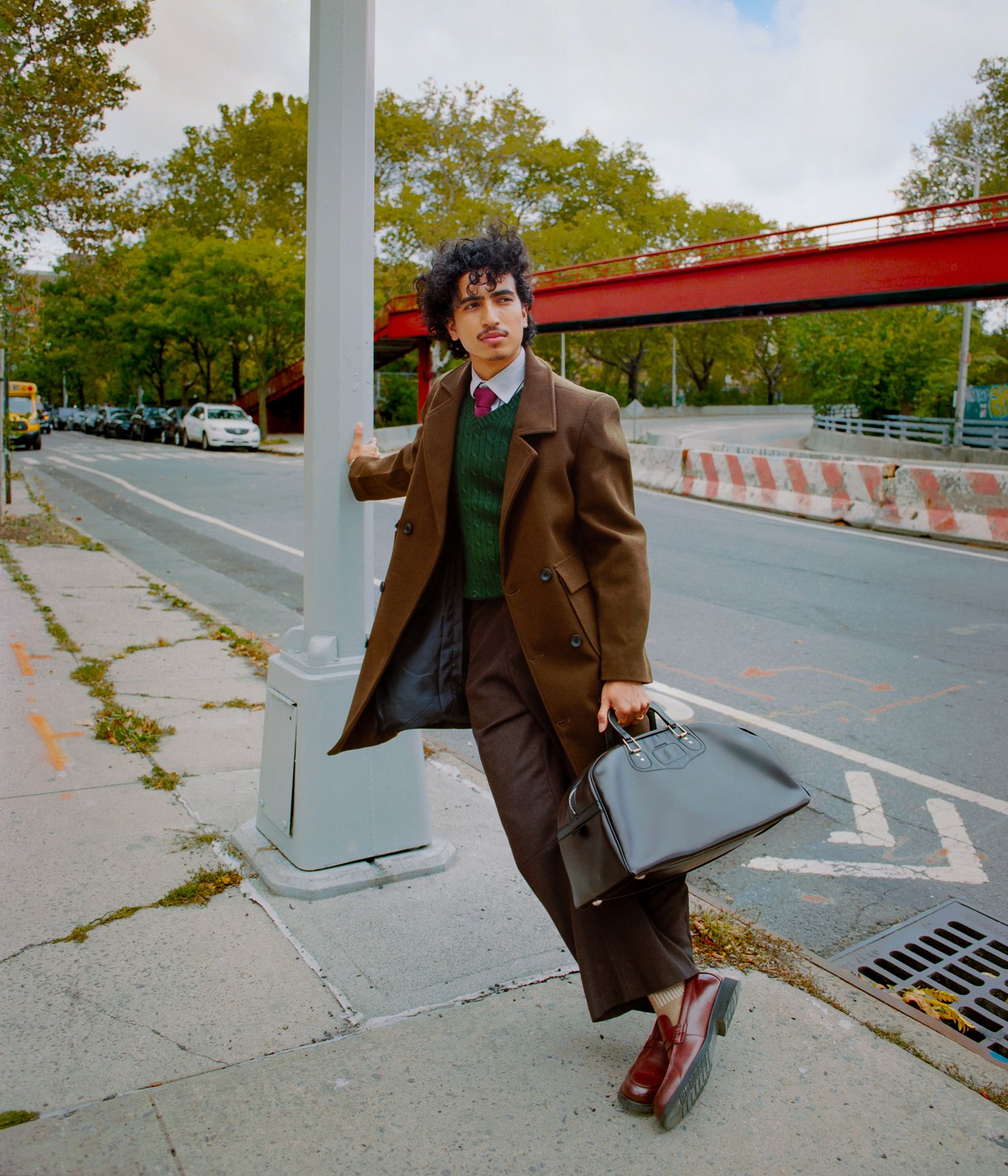 Figure in a brown suit walks through an urban area with concrete barriers and poles.