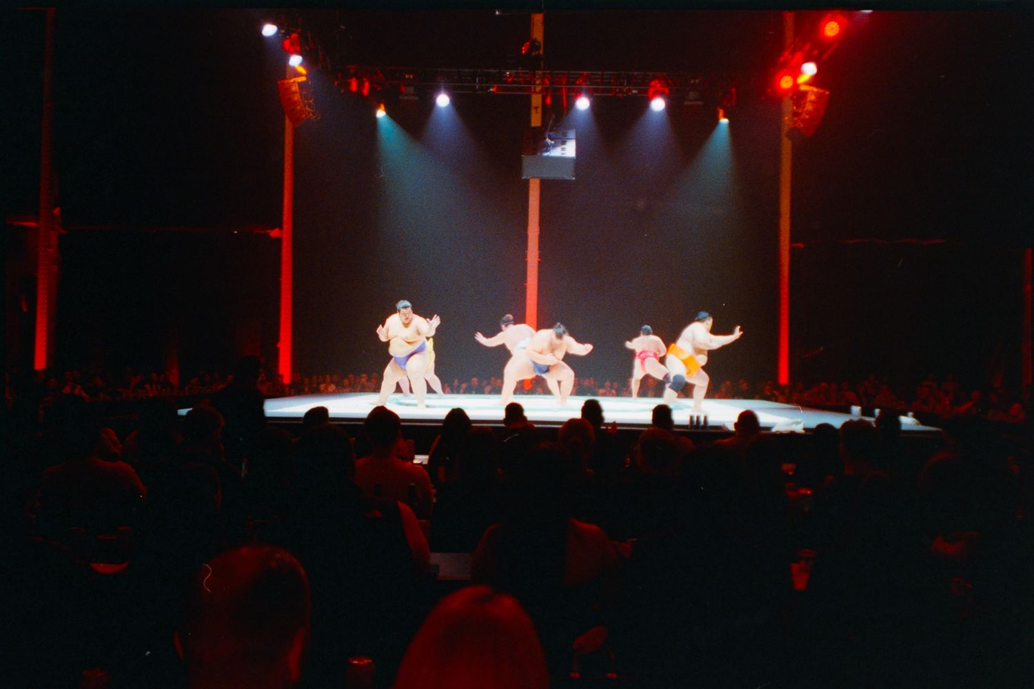 Performers in white costumes on a stage with red pillars and dramatic lighting before a live audience.