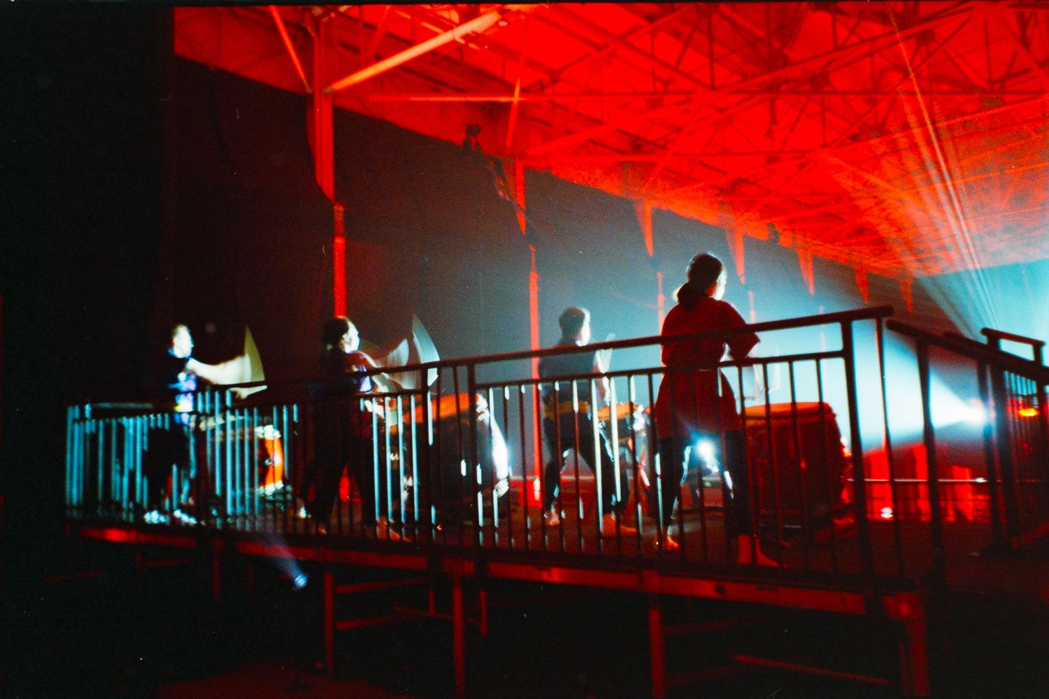 Performers on an elevated platform bathed in dramatic red and blue stage lighting during a live concert event.