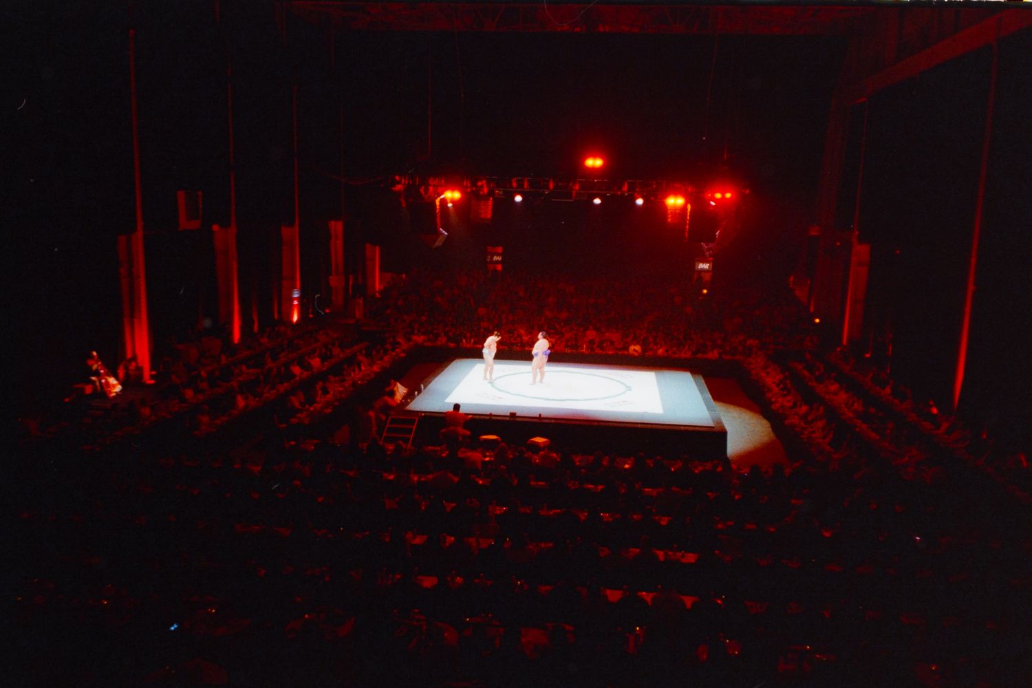 Aerial view of a theater stage glowing white under spotlights, surrounded by red-lit seating in a dark auditorium.