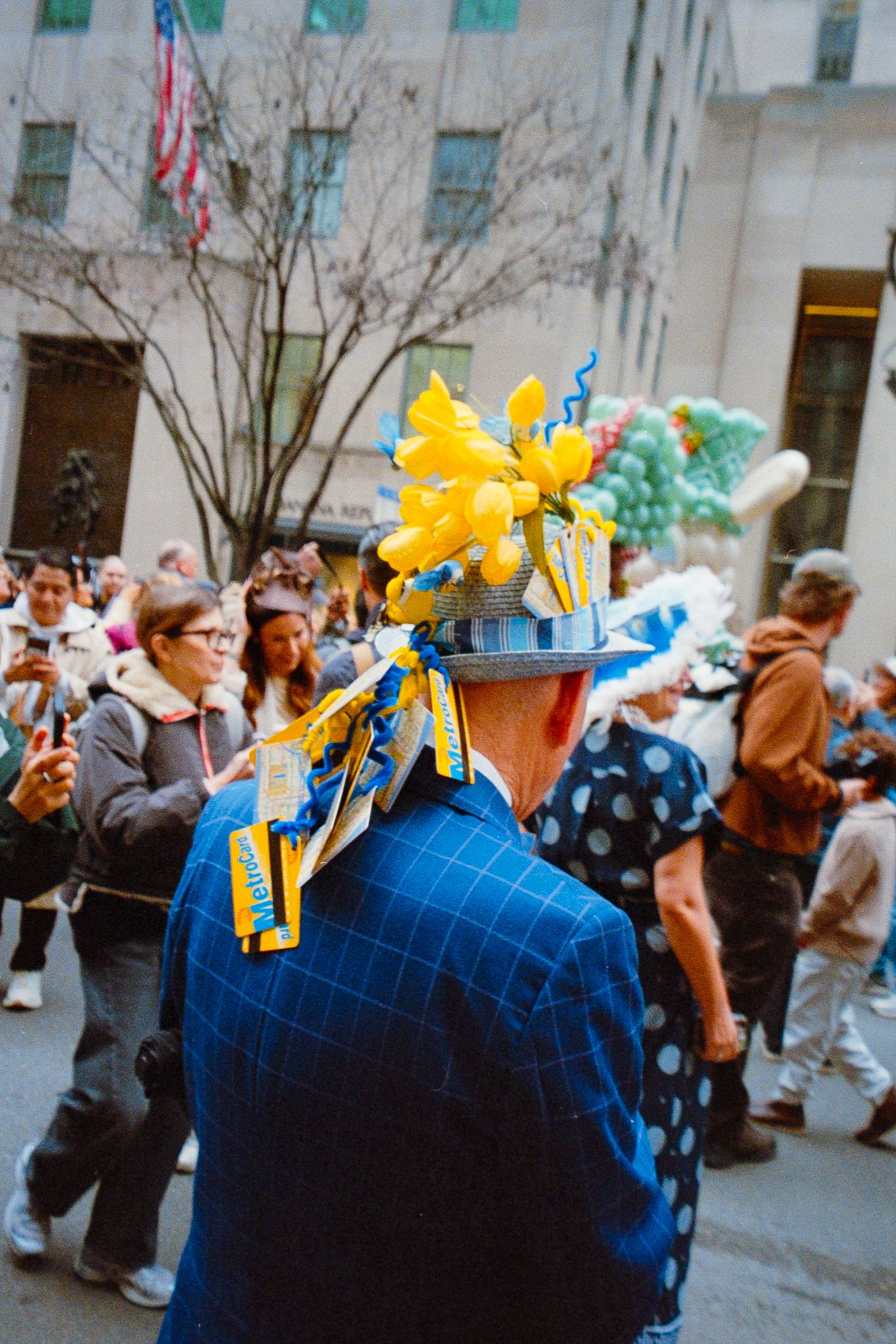 Person wearing colorful Easter bonnet with yellow flowers at a festive New York City street parade.