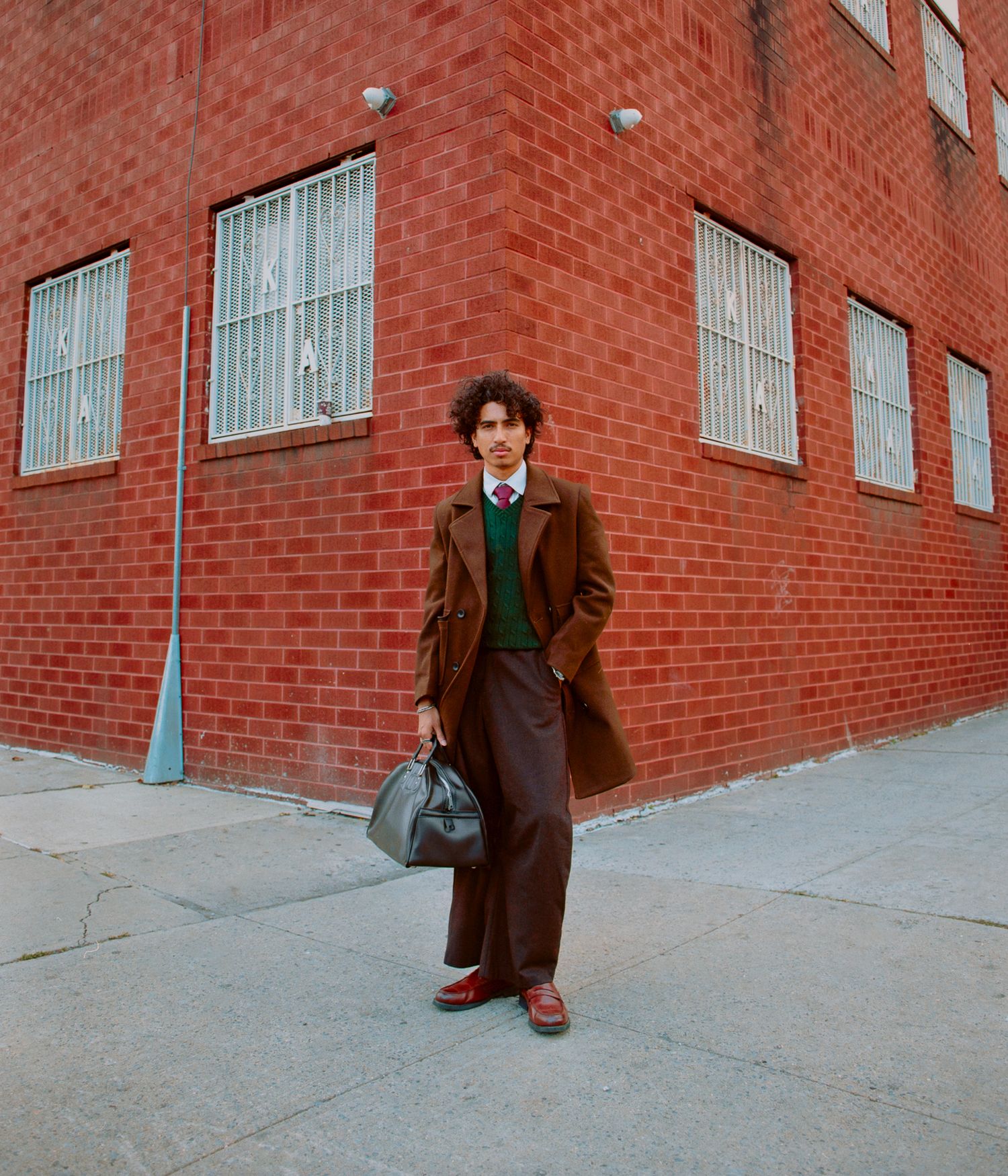 Person in brown coat walking past red brick building wall on urban sidewalk.