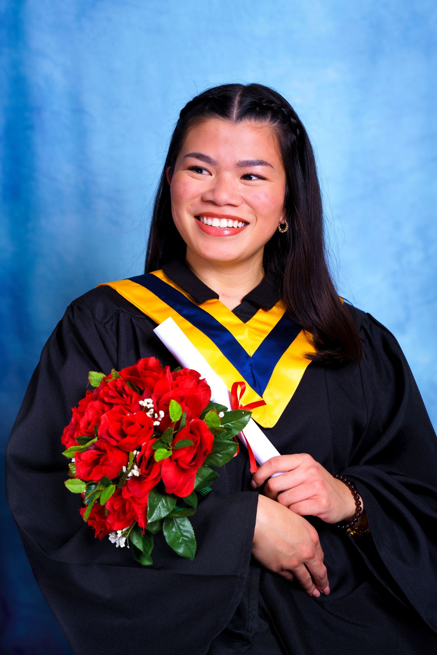 Graduate poses with red bouquet in black academic gown with gold and blue trim.