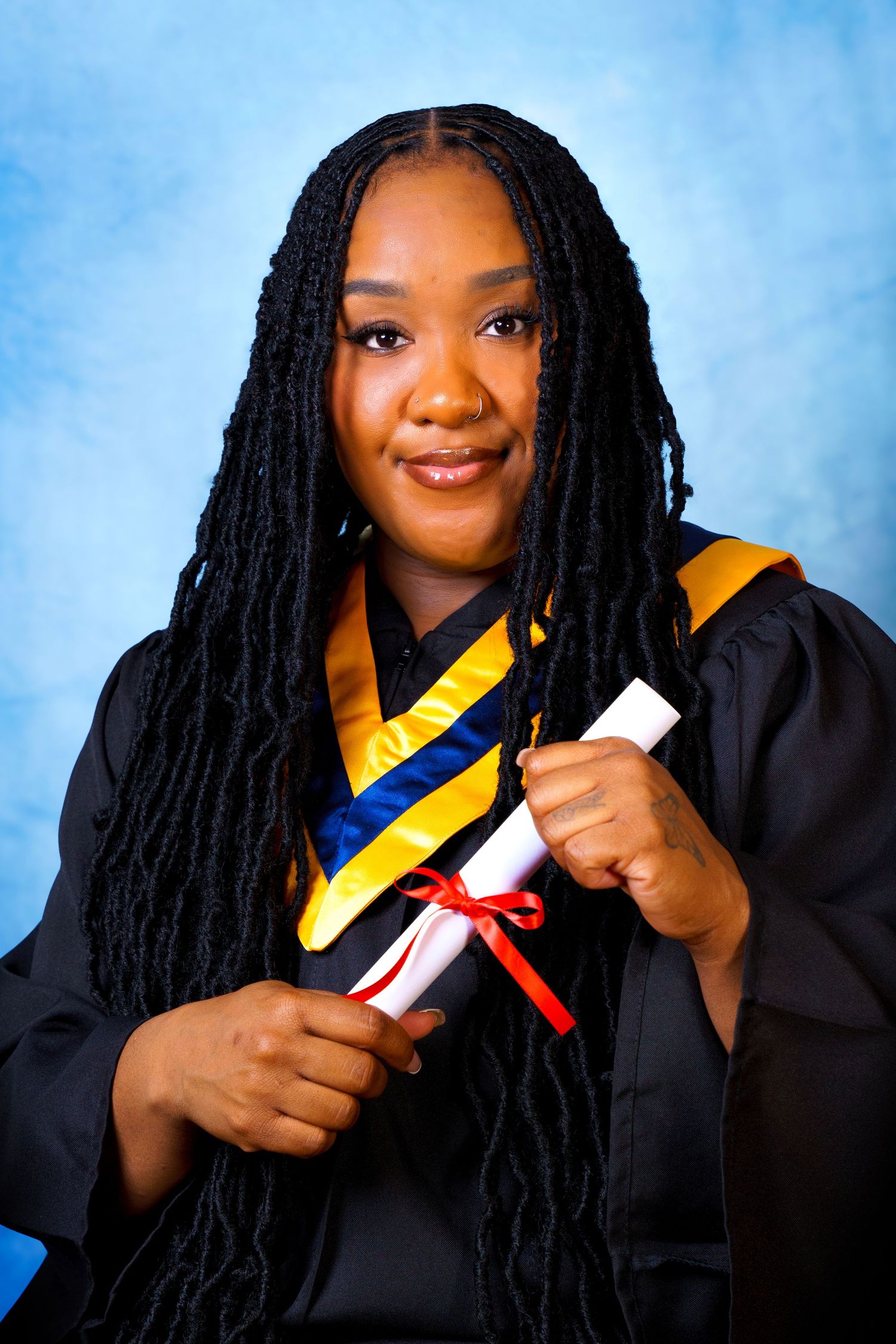 Graduate in cap and gown holding diploma against blue backdrop.