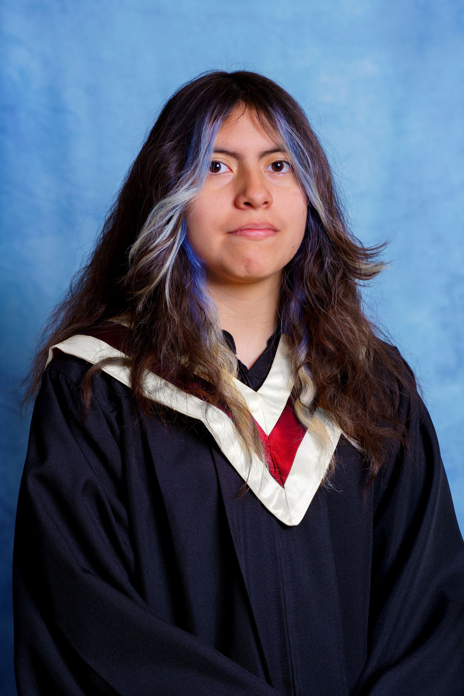 Graduate in black academic dress with white and red trim poses against blue background.