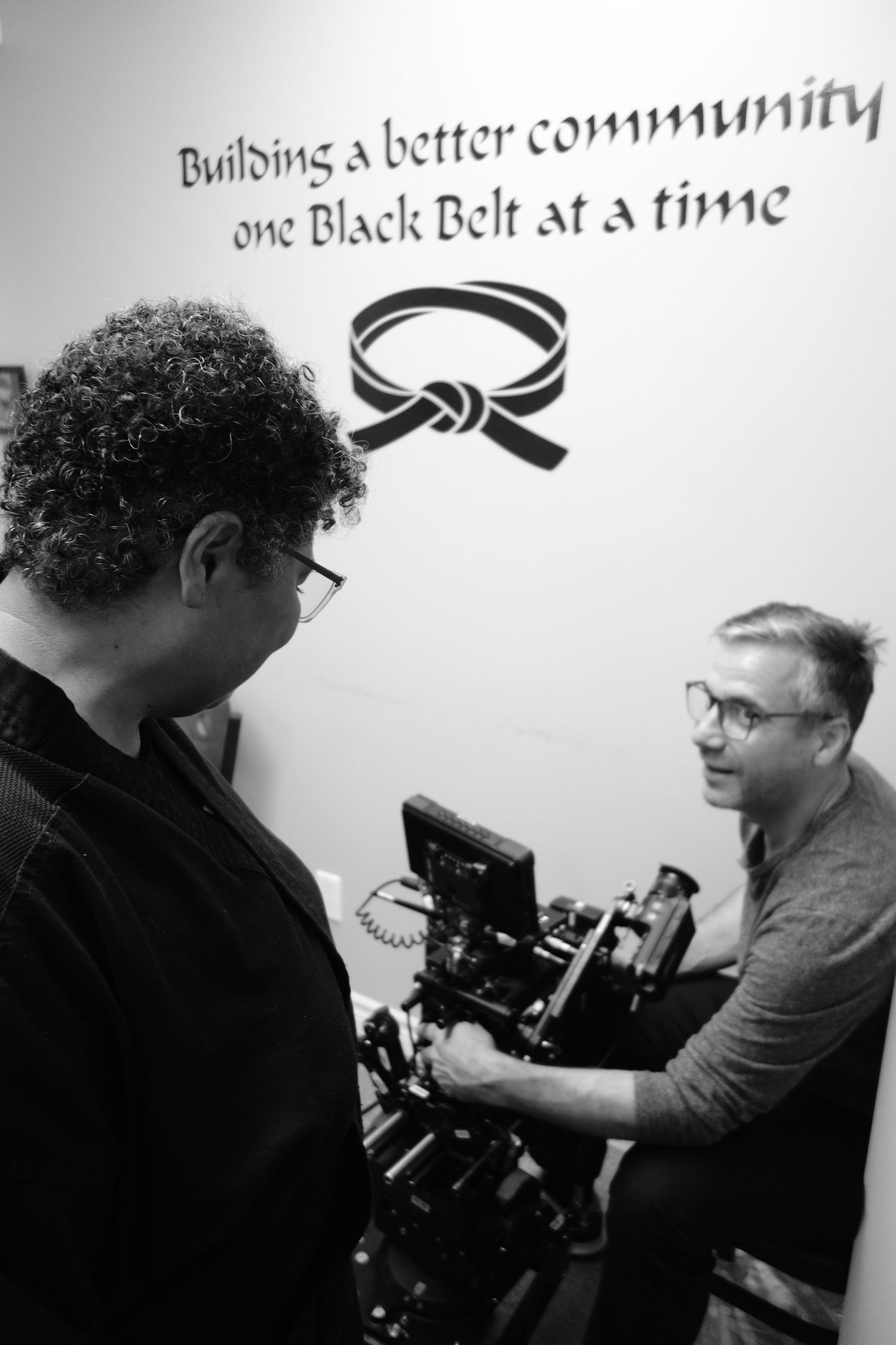 Behind the scenes footage being filmed in a martial arts studio showing camera equipment and text about black belts.