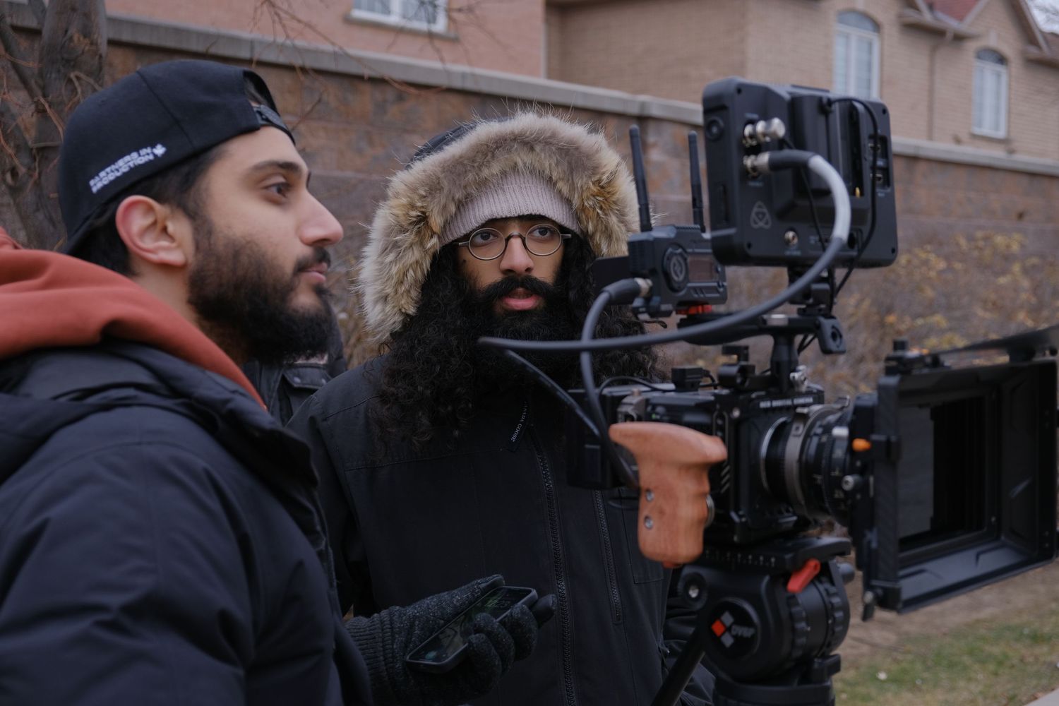 Two camera operators filming with professional equipment in winter coats outdoors.