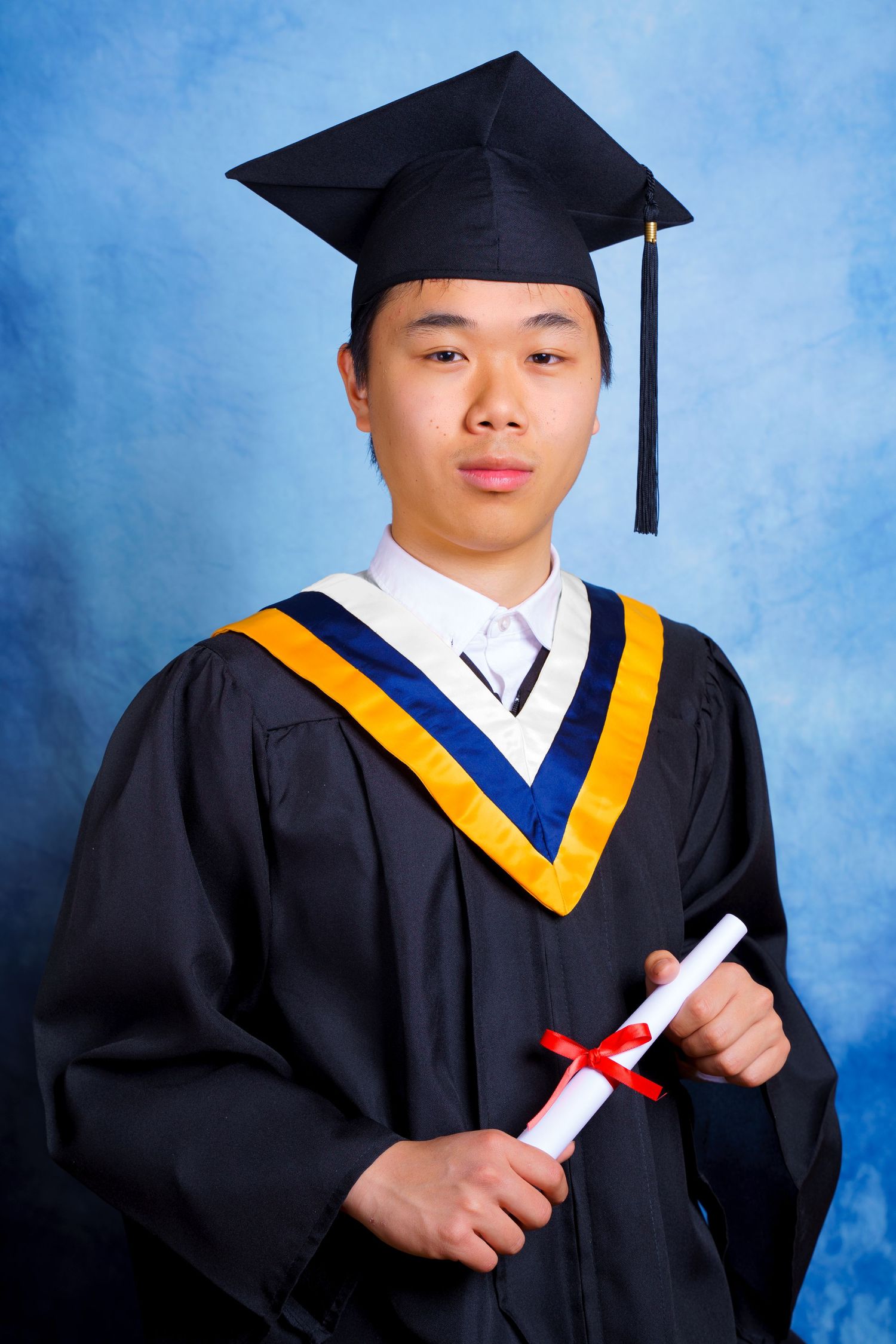 Graduate in cap and gown displays diploma against blue studio backdrop.