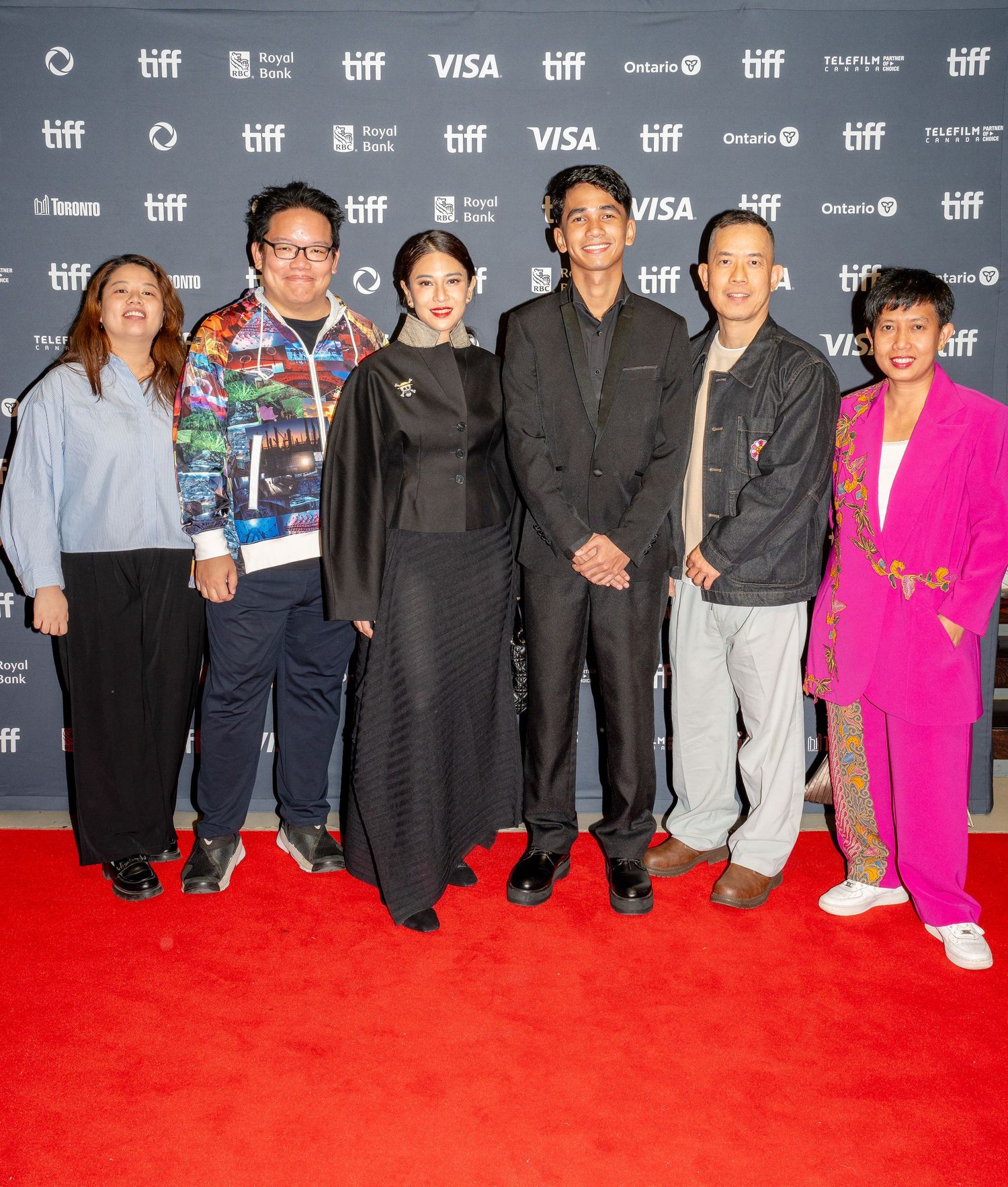 Group of people posing together on red carpet at TIFF film festival with sponsors backdrop.
