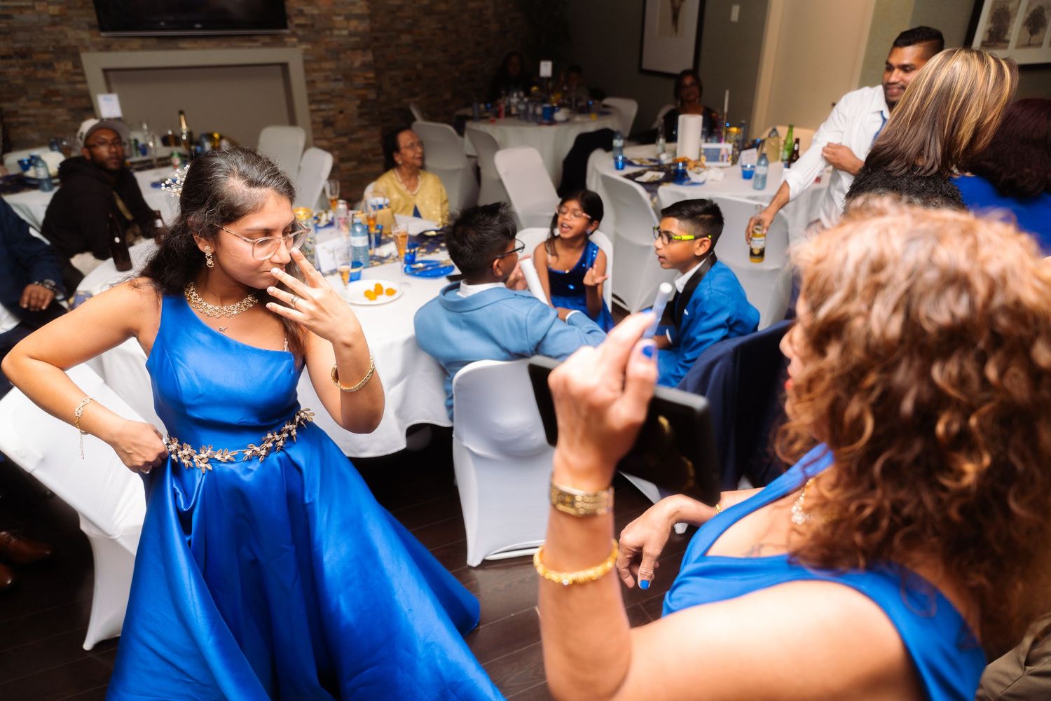 Wedding guests in royal blue dresses dance and celebrate at a reception party.