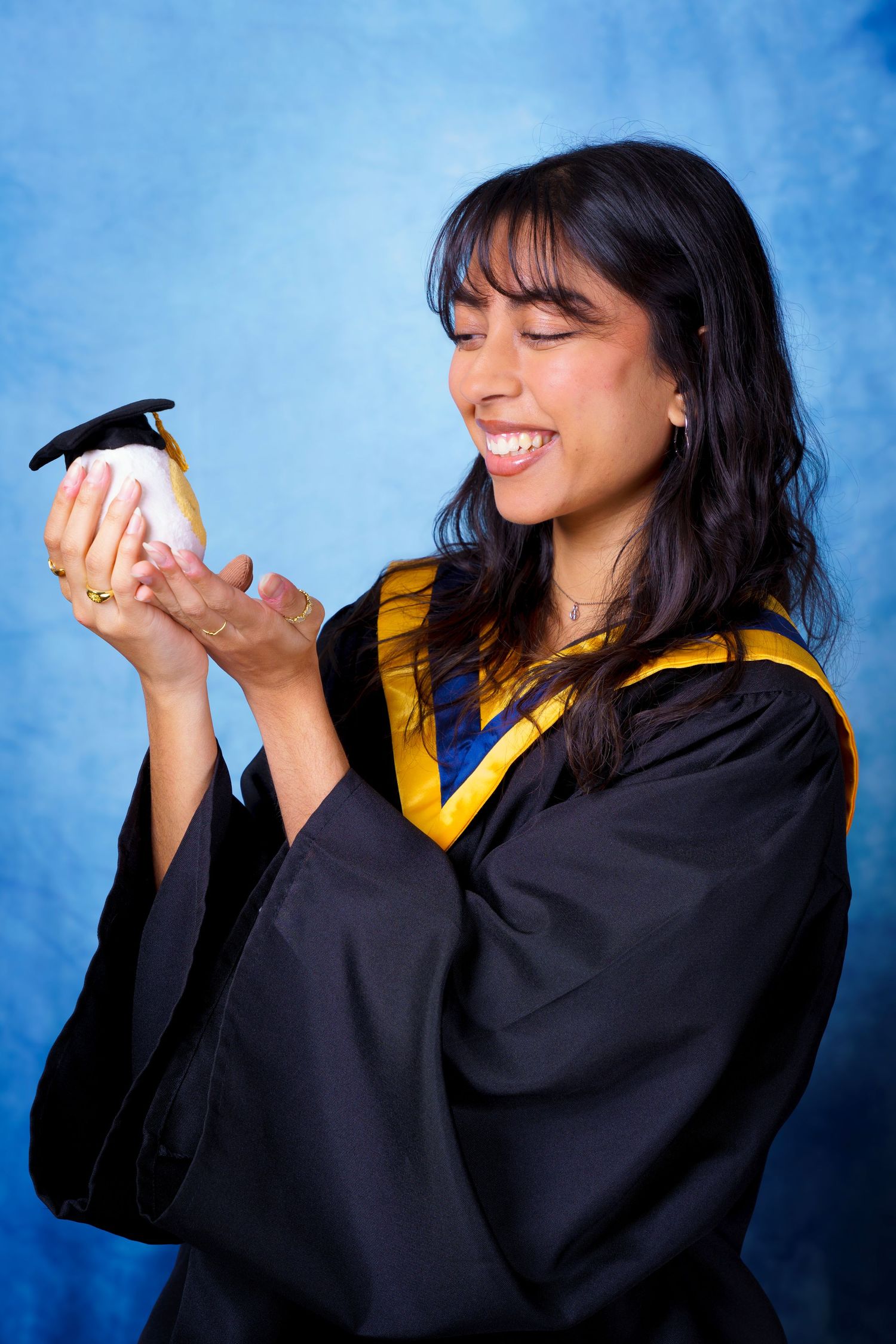 Graduate poses playfully with diploma in black graduation gown with gold trim.