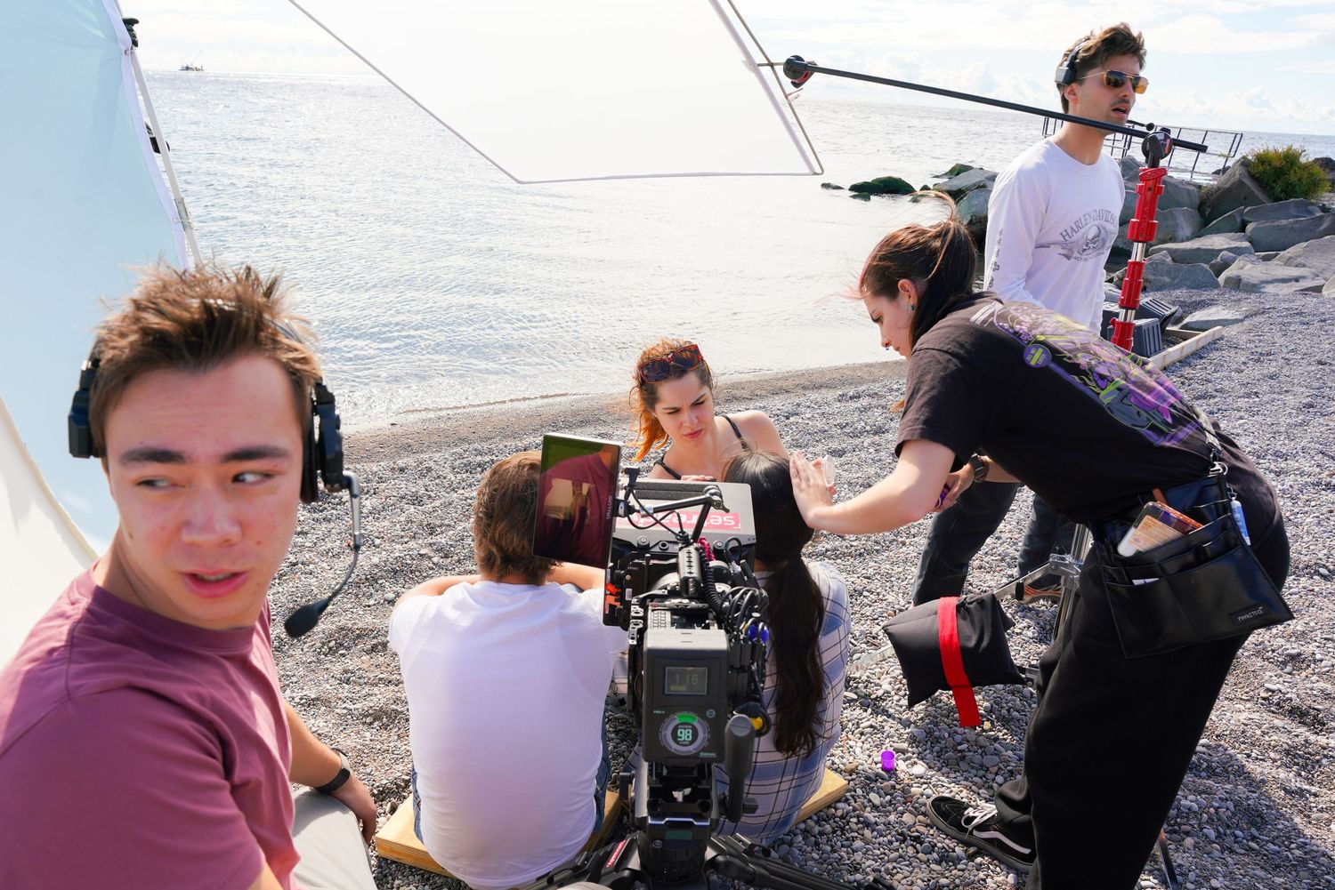 Group of people with camera equipment filming outdoors by the water.