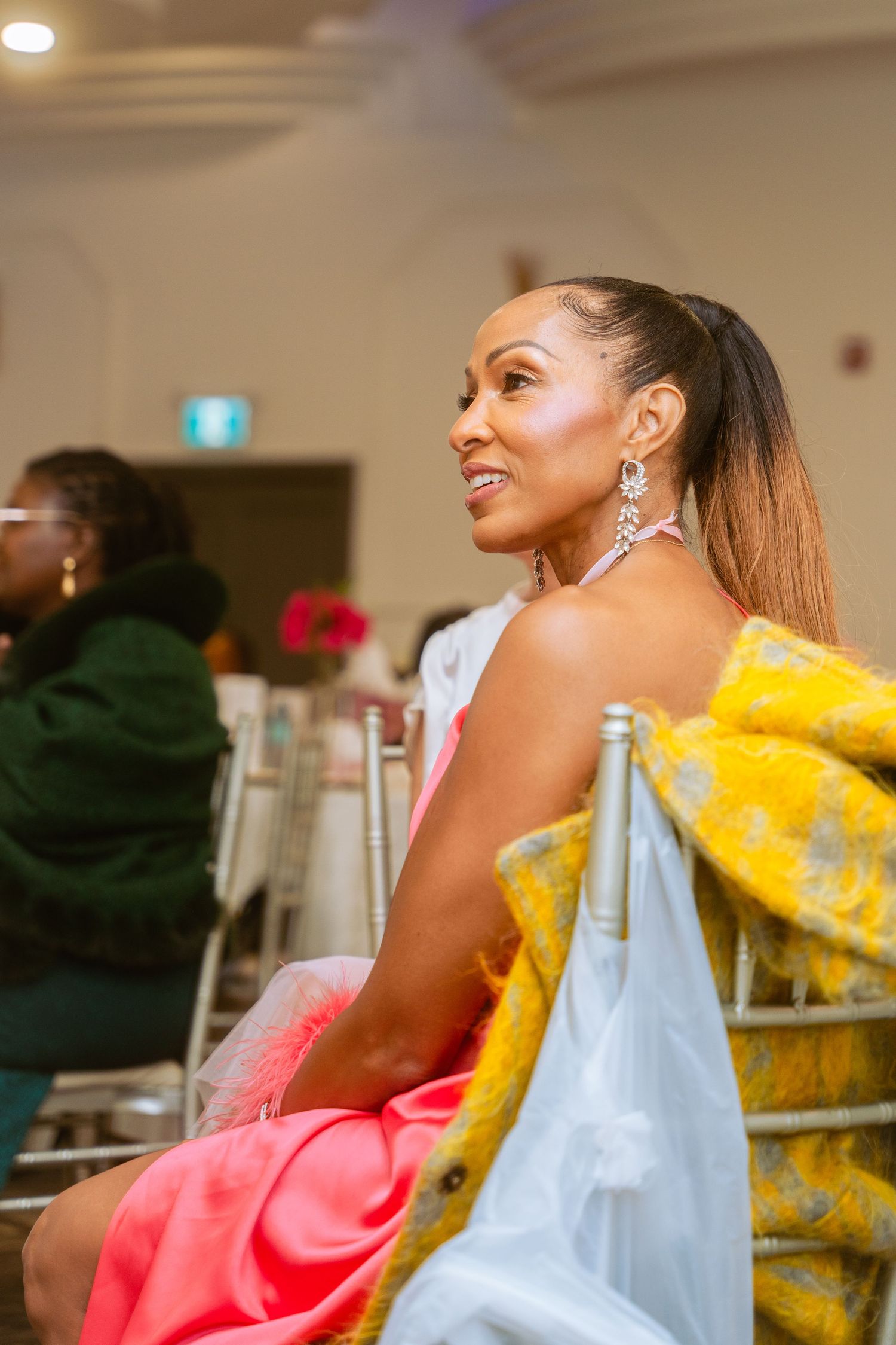 Woman in bright pink outfit with yellow and blue accessories at an indoor celebration.