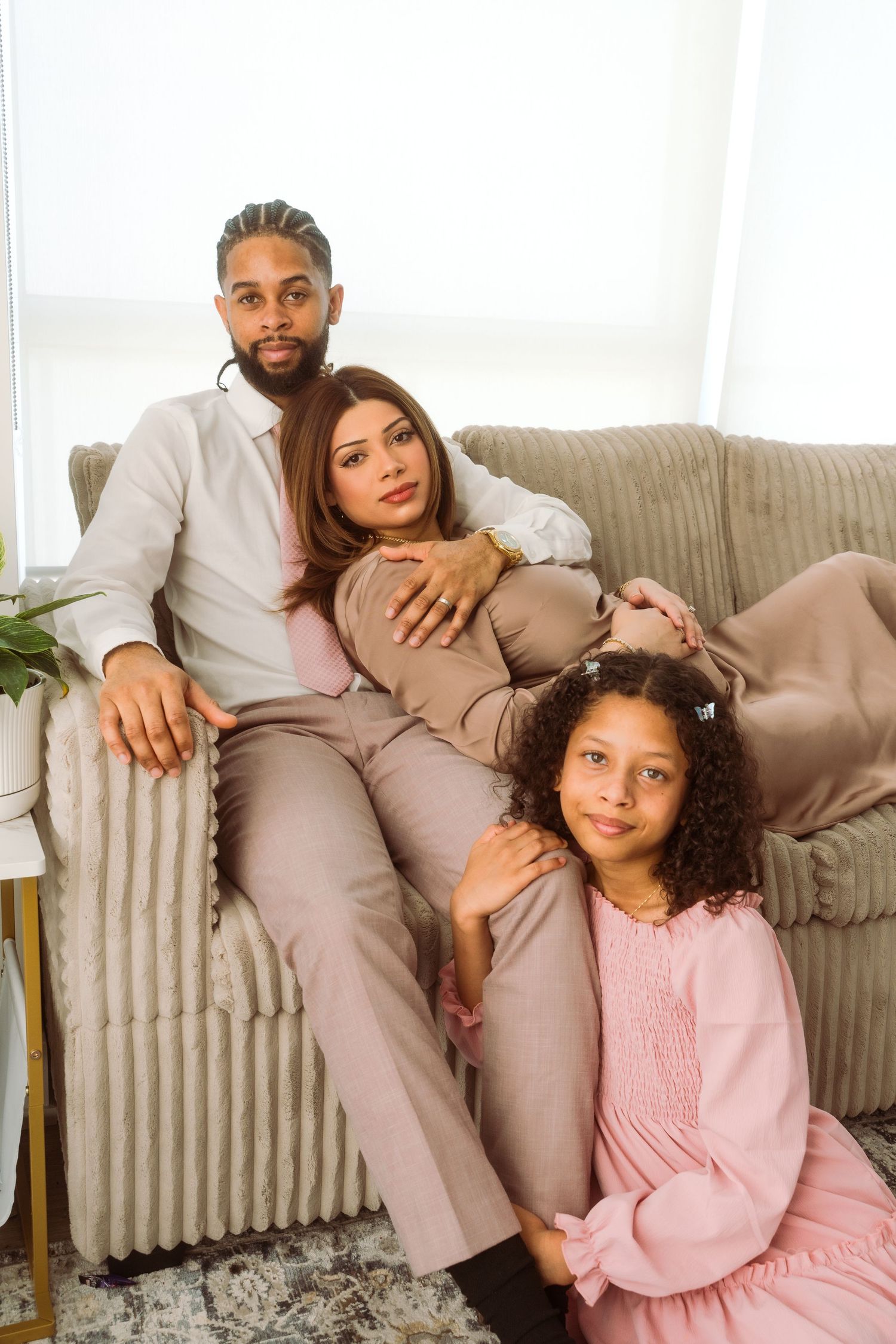 A family in coordinated beige and pink outfits relaxes together on a cozy sofa at home.