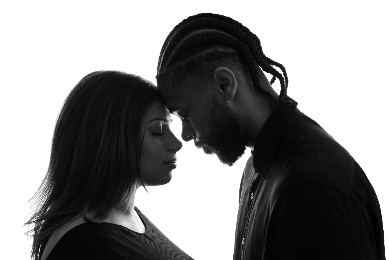 Silhouette of a couple facing each other intimately against white background in dramatic black and white contrast.