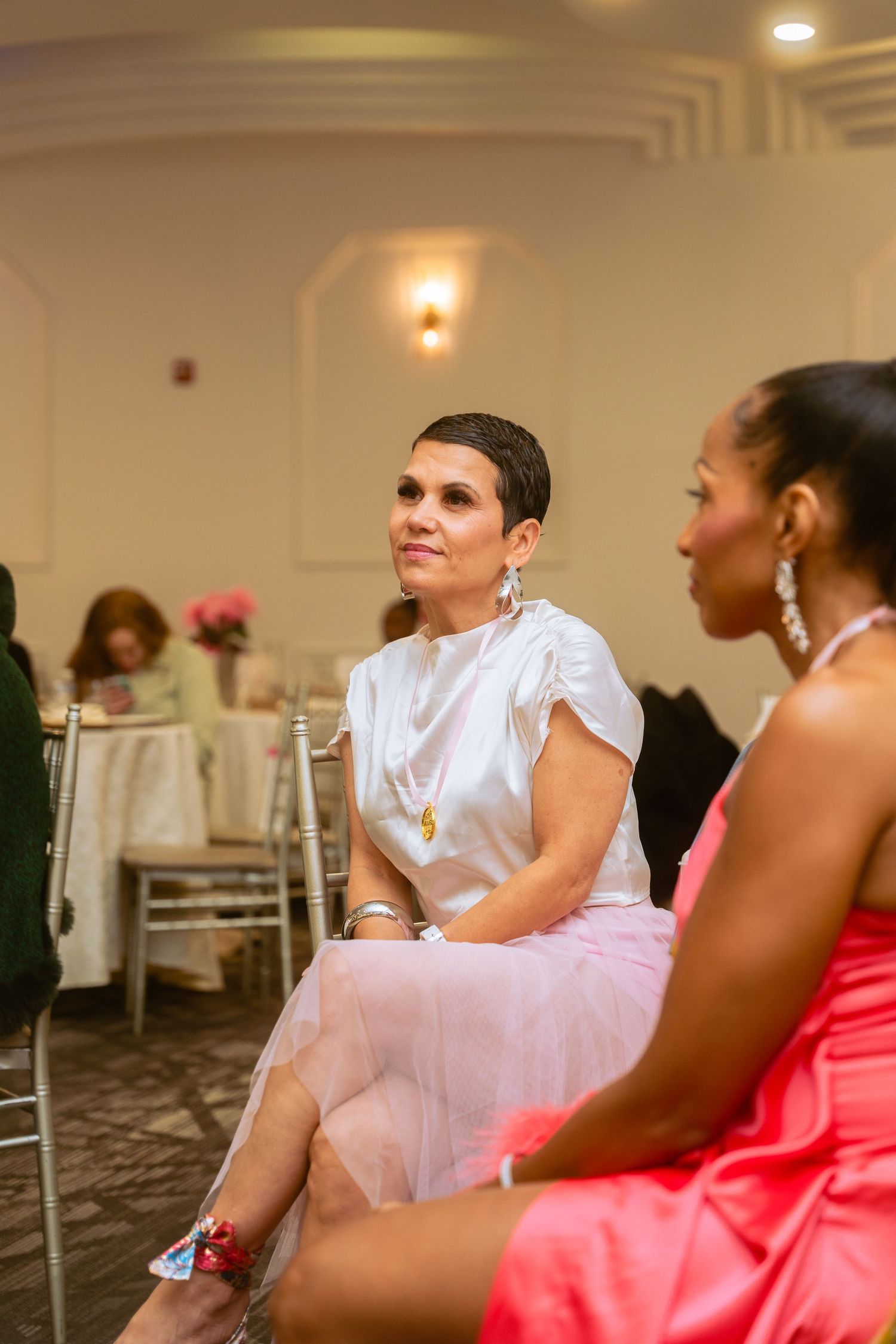 Guests in formal attire seated at an elegant indoor event venue with white decor.
