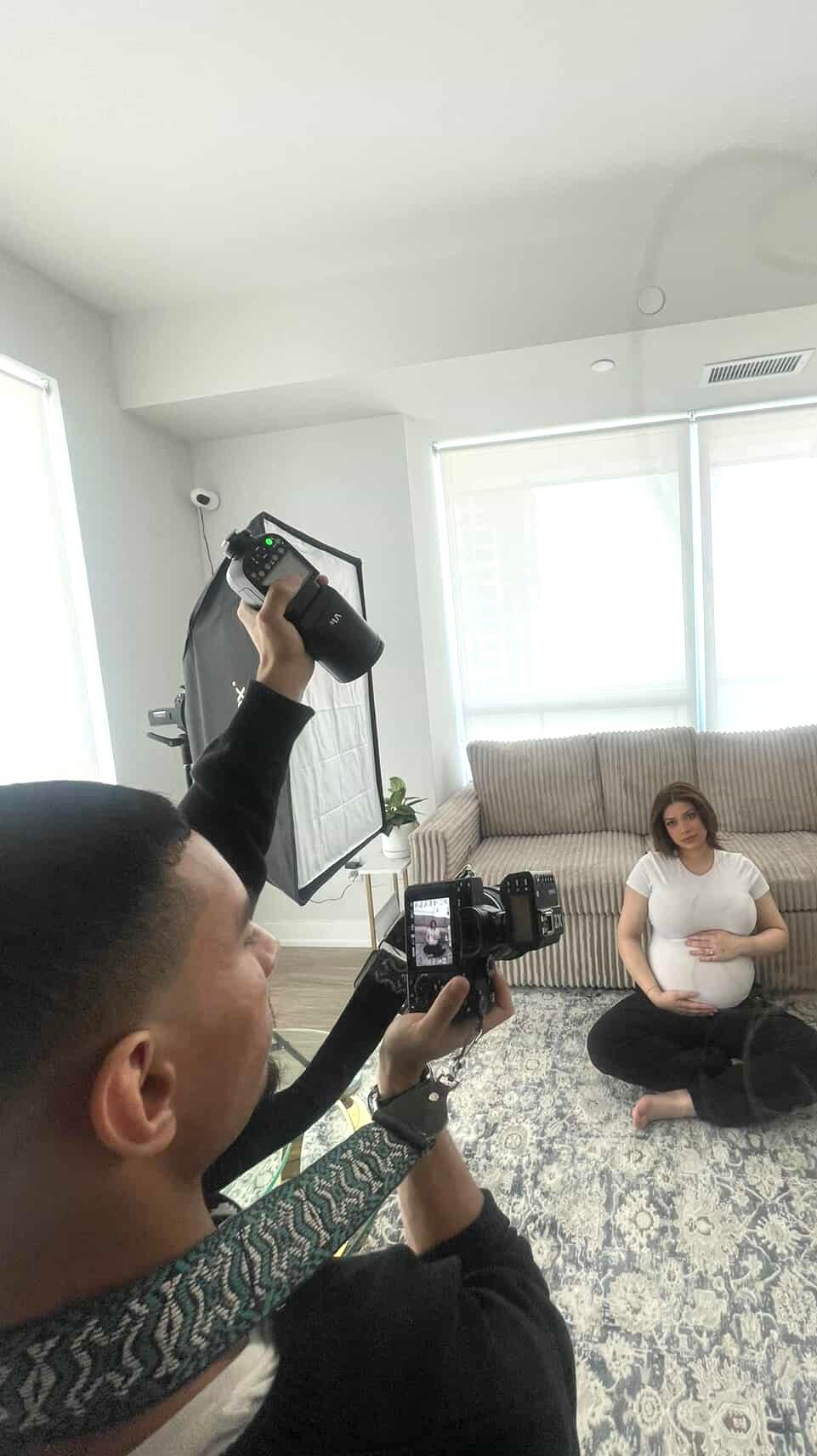 Behind-the-scenes of maternity photoshoot with photographer using lighting equipment.