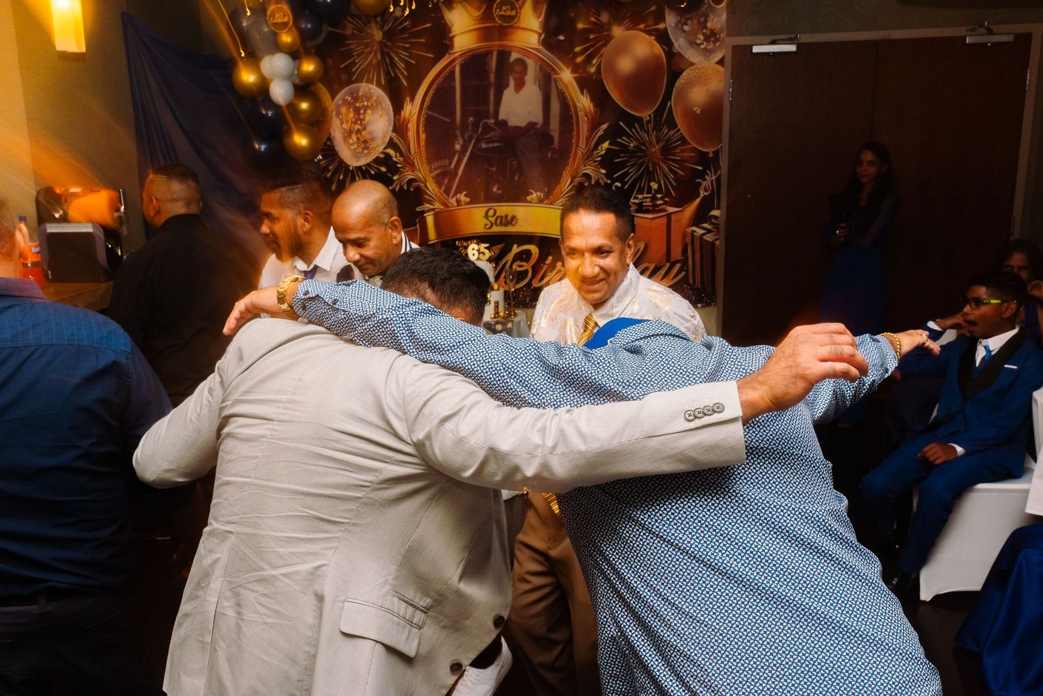 Group of men in formal attire embracing in a celebratory huddle at a party.