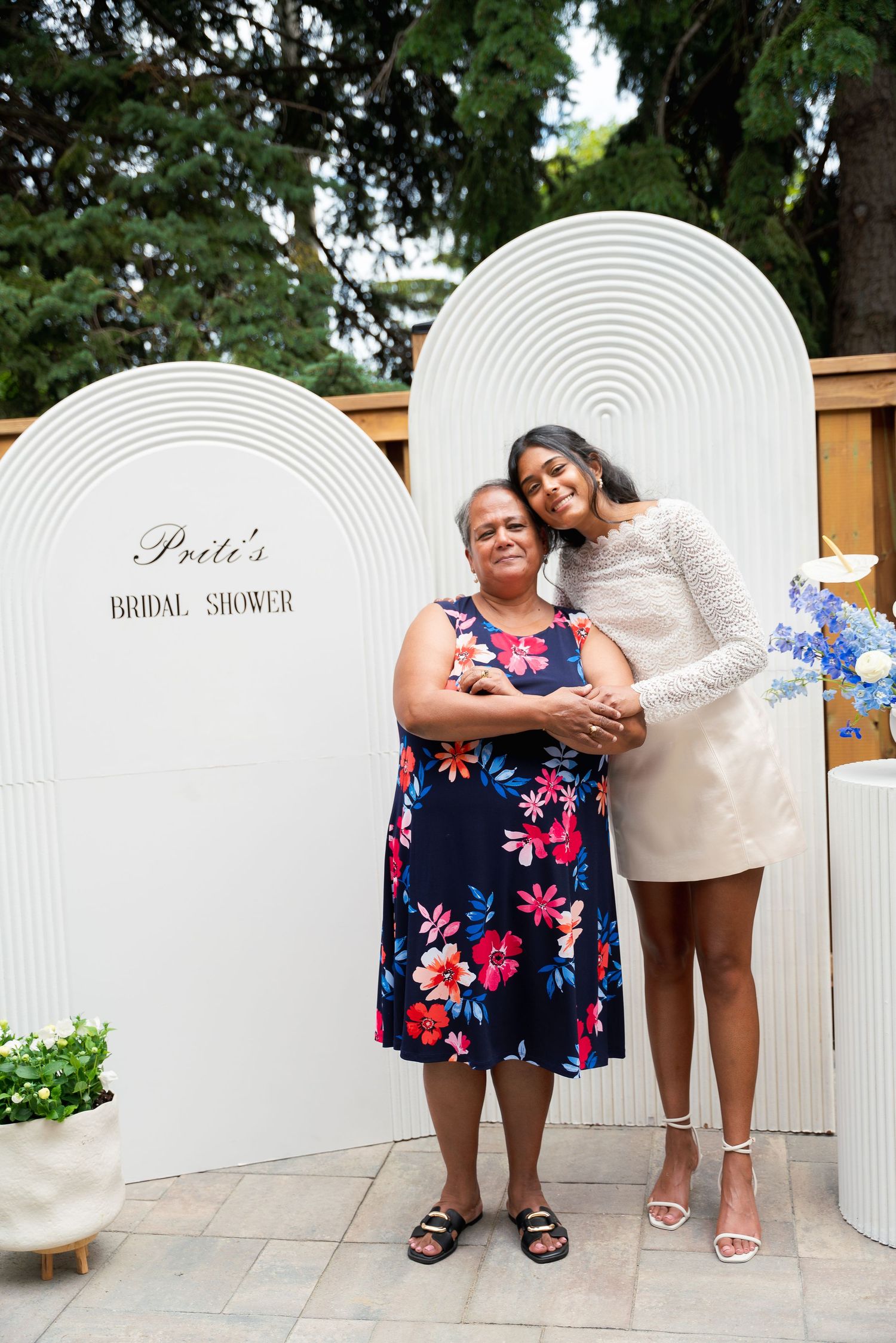 A joyful bridal shower celebration with floral decorations and white backdrop panels in an outdoor garden setting.