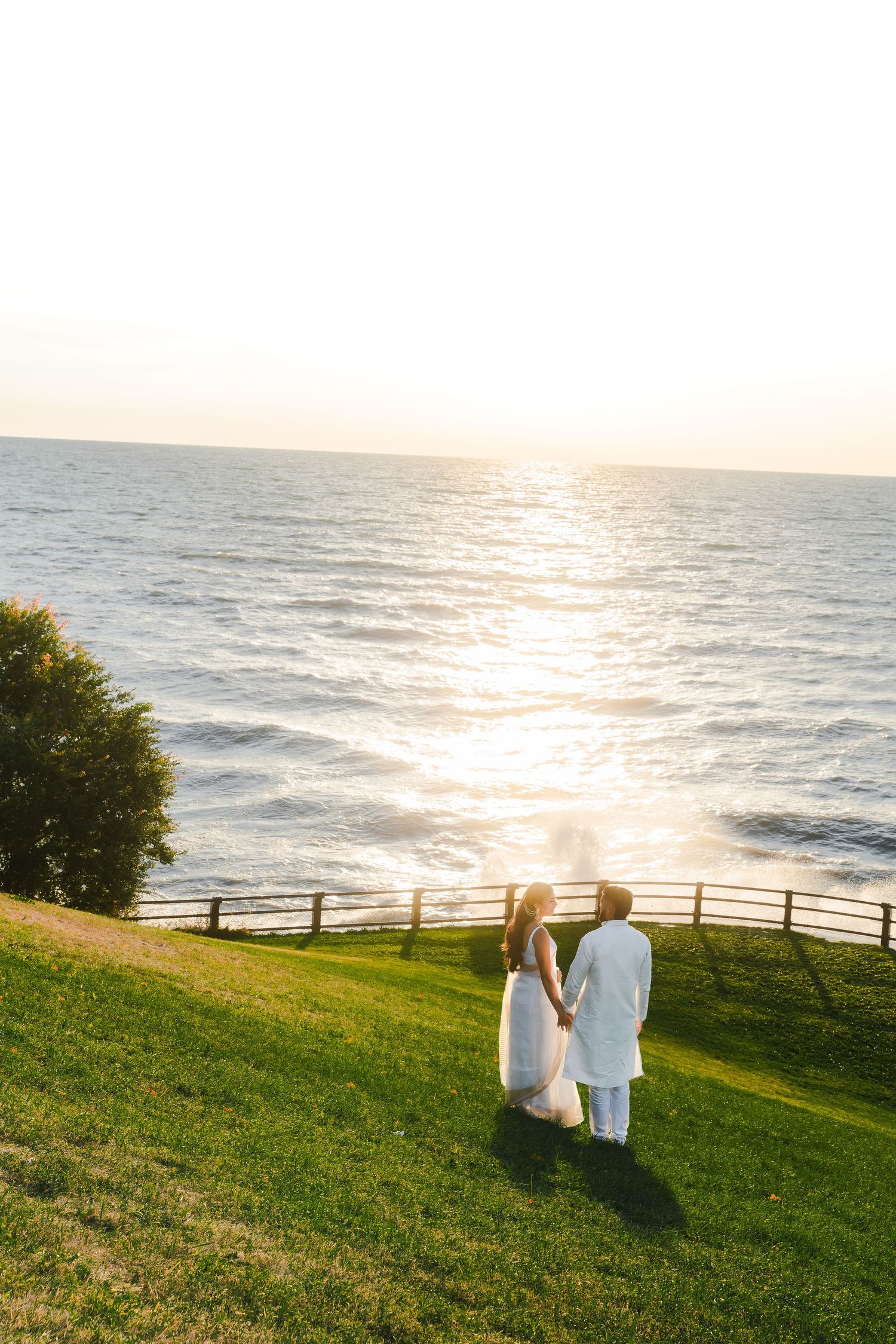 Scenic coastal landscape with couple walking on grassy hill overlooking ocean at sunset.