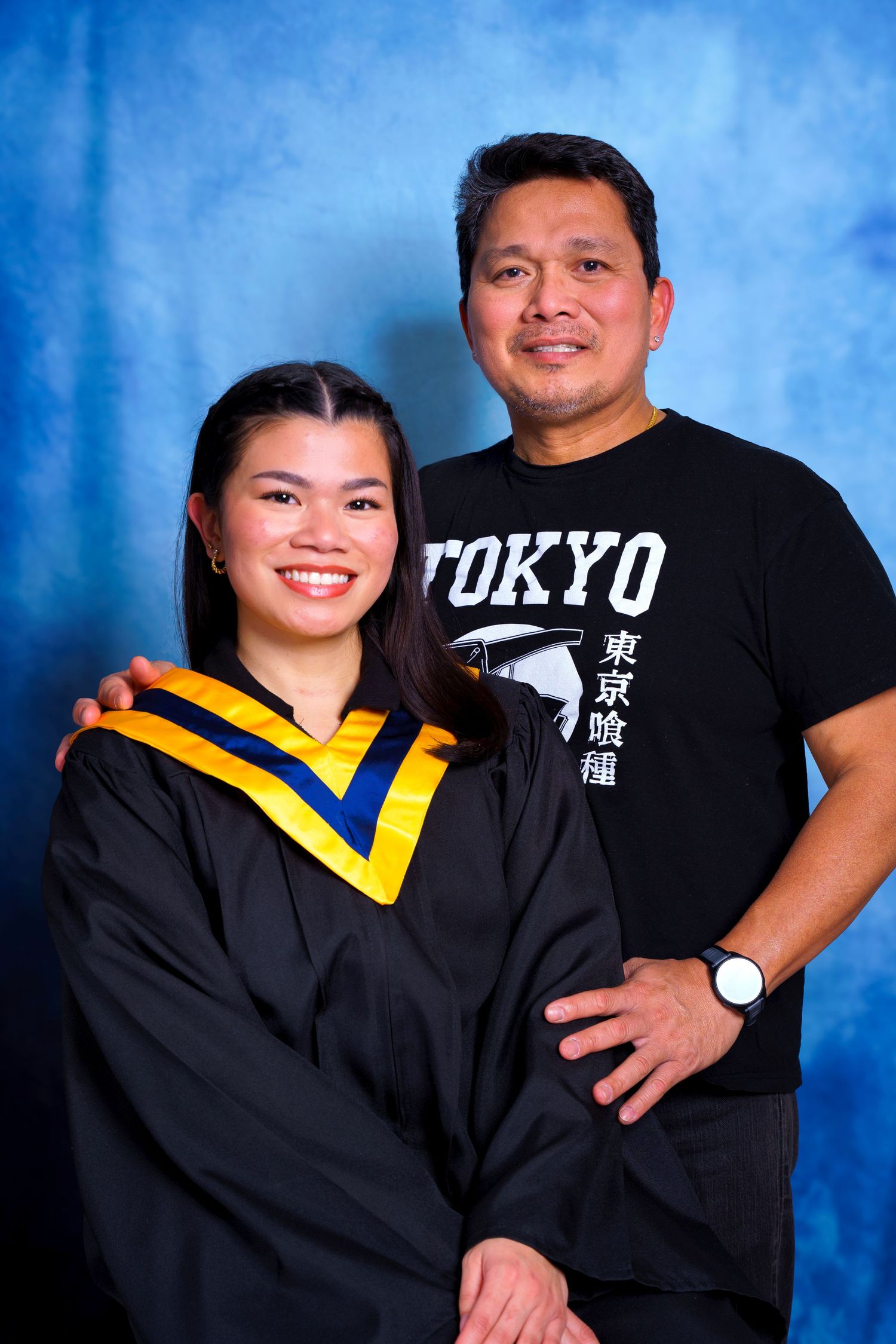 Graduate in academic regalia poses with family member wearing Tokyo graphic t-shirt.