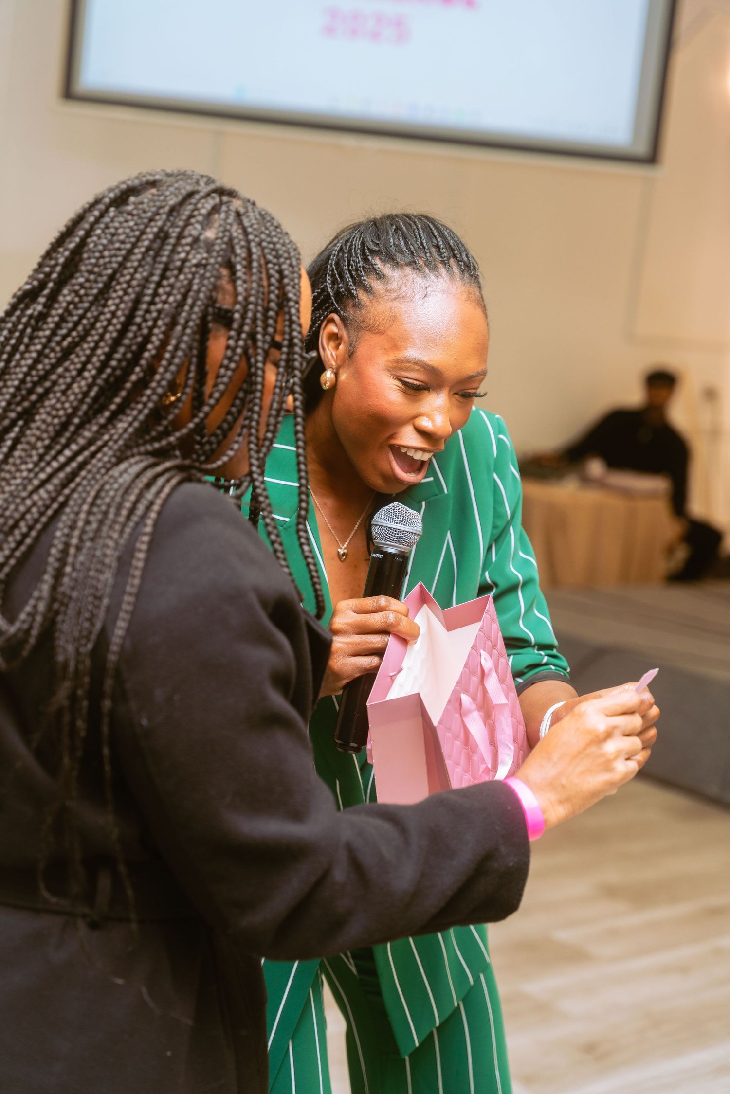 Two people in green and pink outfits share an enthusiastic interaction at an indoor venue.