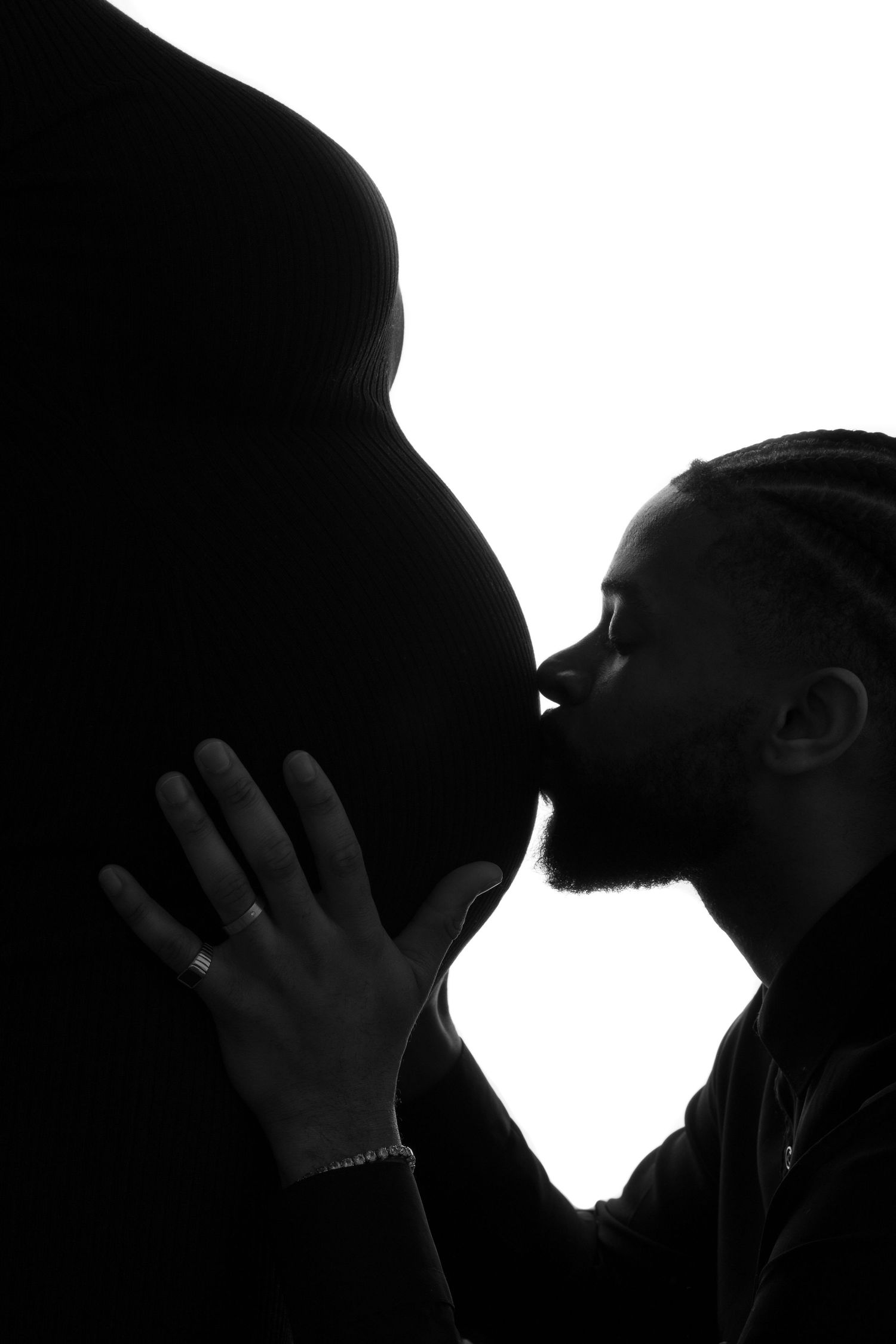 A silhouetted figure kisses a pregnant belly in this intimate black and white maternity portrait.