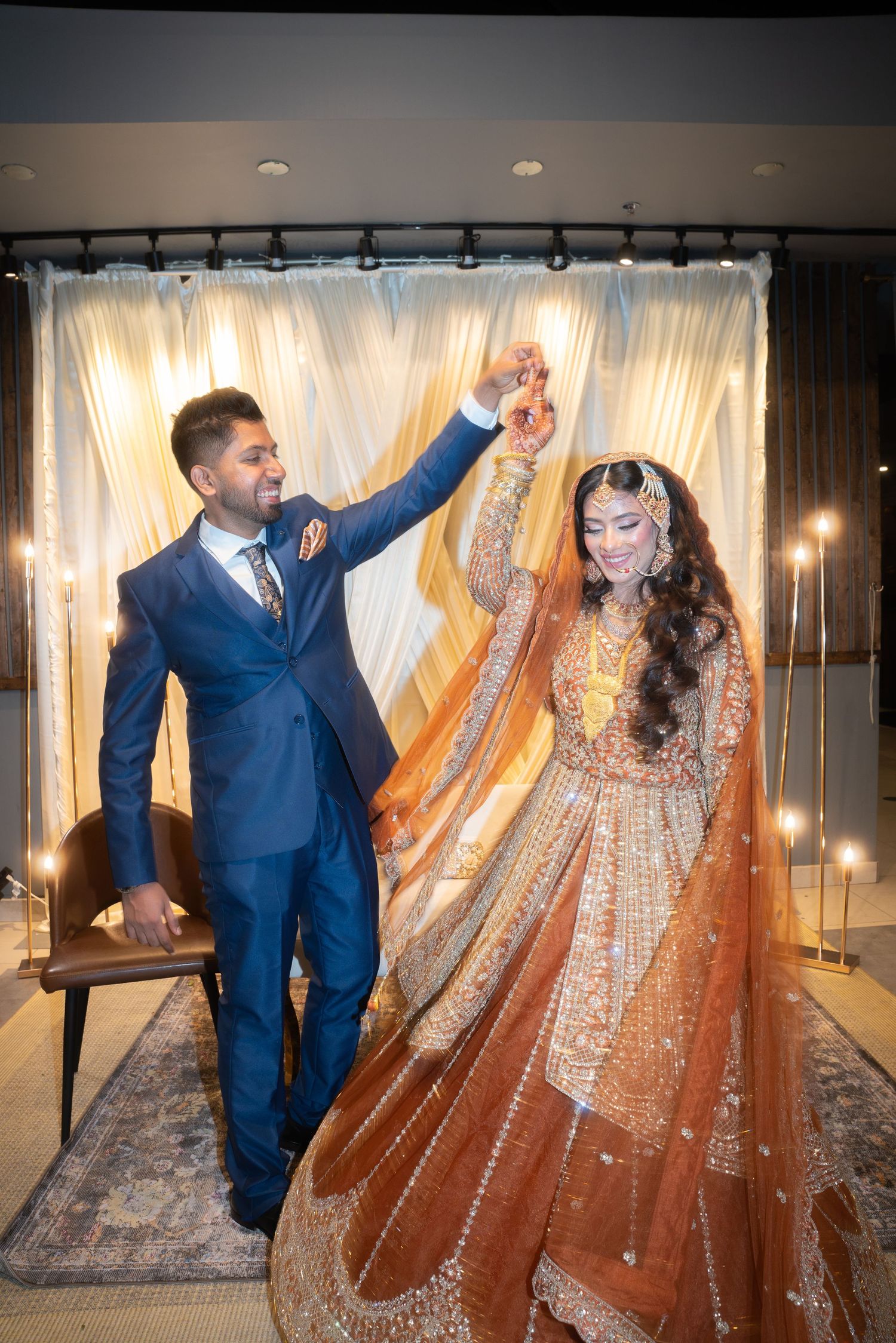 A couple dancing in formal attire, with the bride wearing an ornate orange and gold lehenga.